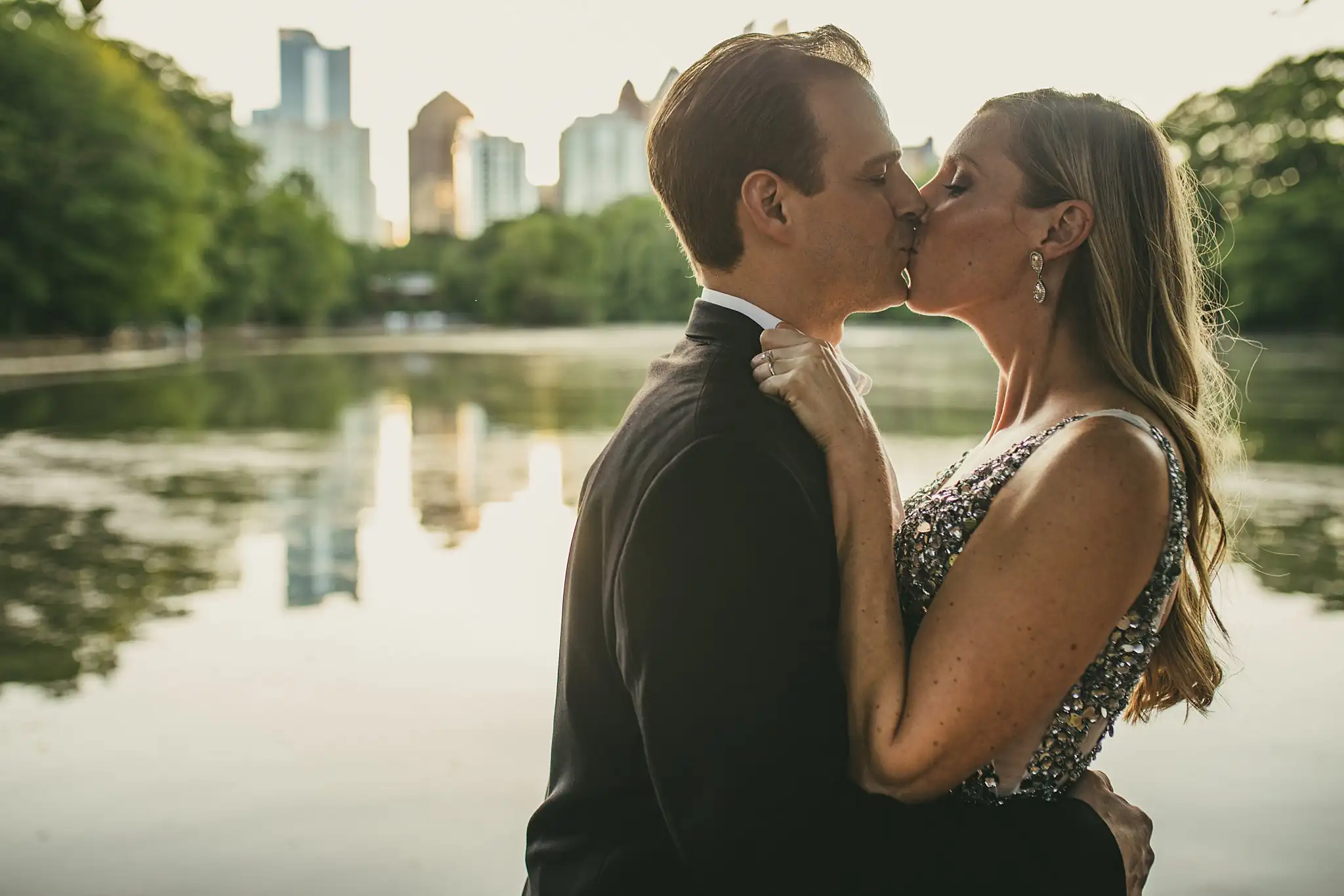 AtlantaWeddingPhotographers_0354.jpg Engagement Portraits: a kiss with the lake and the city behind them, during their engagement session in Midtown Atlanta, GA
