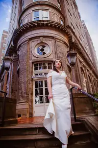 Bridal Portraits: the bride on the steps of a brick corner building, at a wedding