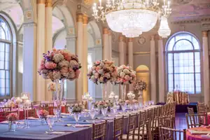 Reception Details: a ballroom laid with tall pink florals under chandeliers, at a wedding