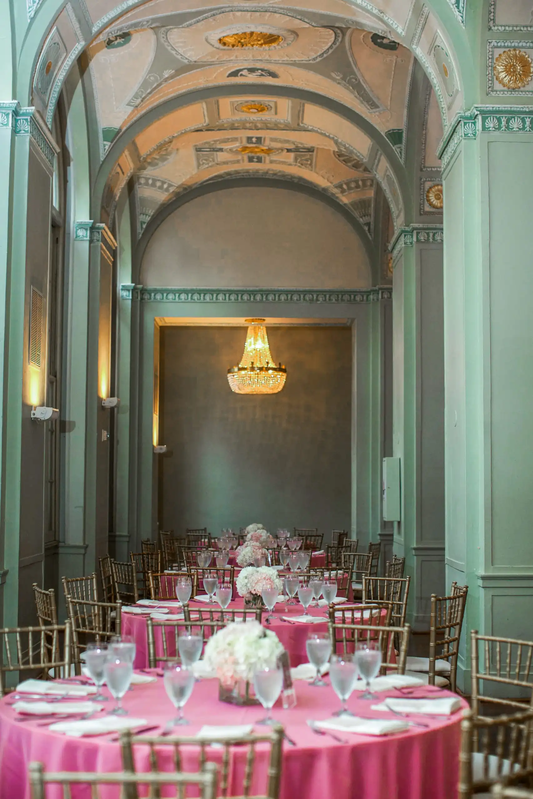 Reception Details: a pale green ballroom laid with pink linen, at a wedding