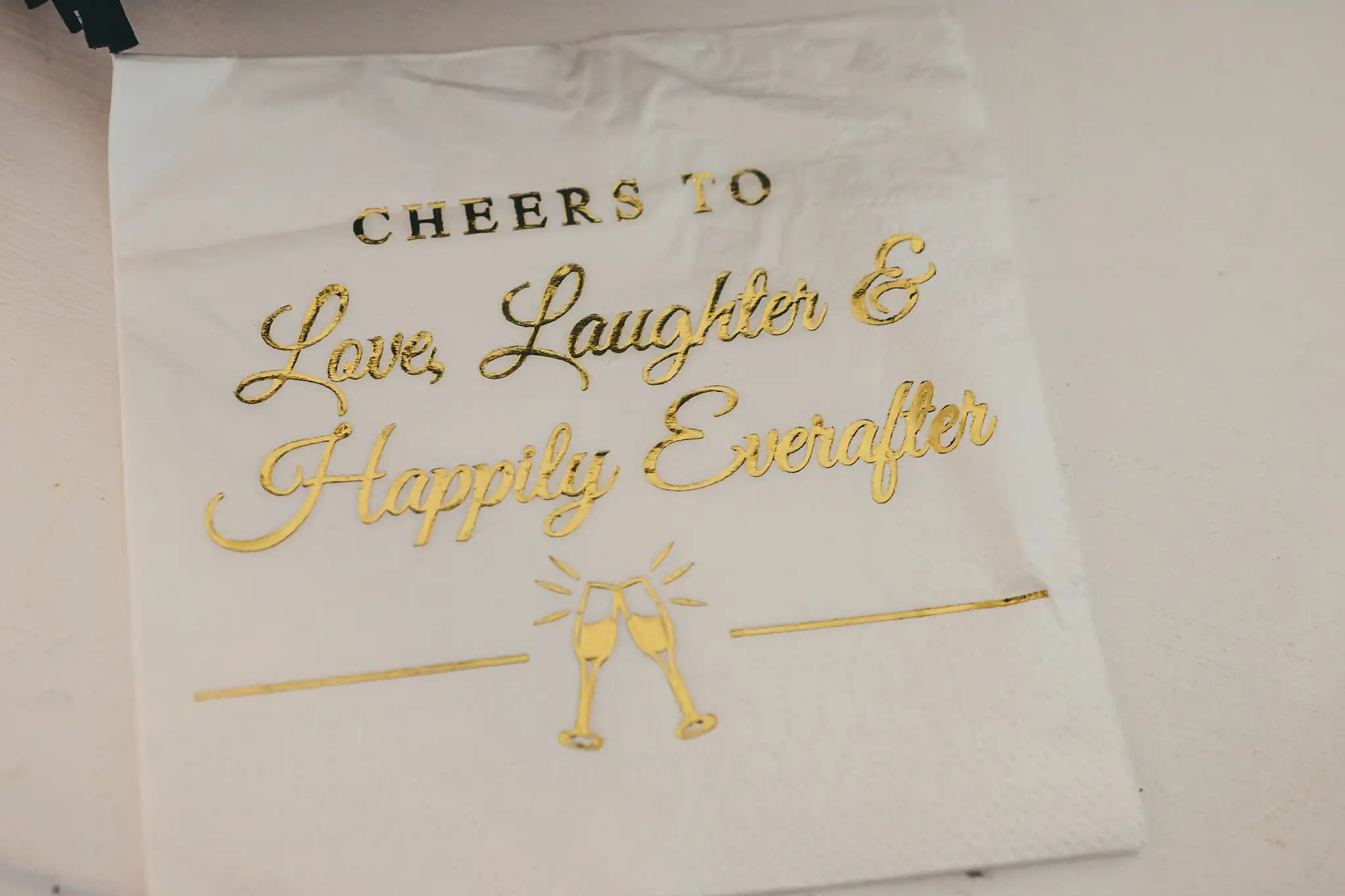 Wedding Details: a napkin lettered Cheers to Love, Laughter, at a wedding at Little River Farms in Milton, GA