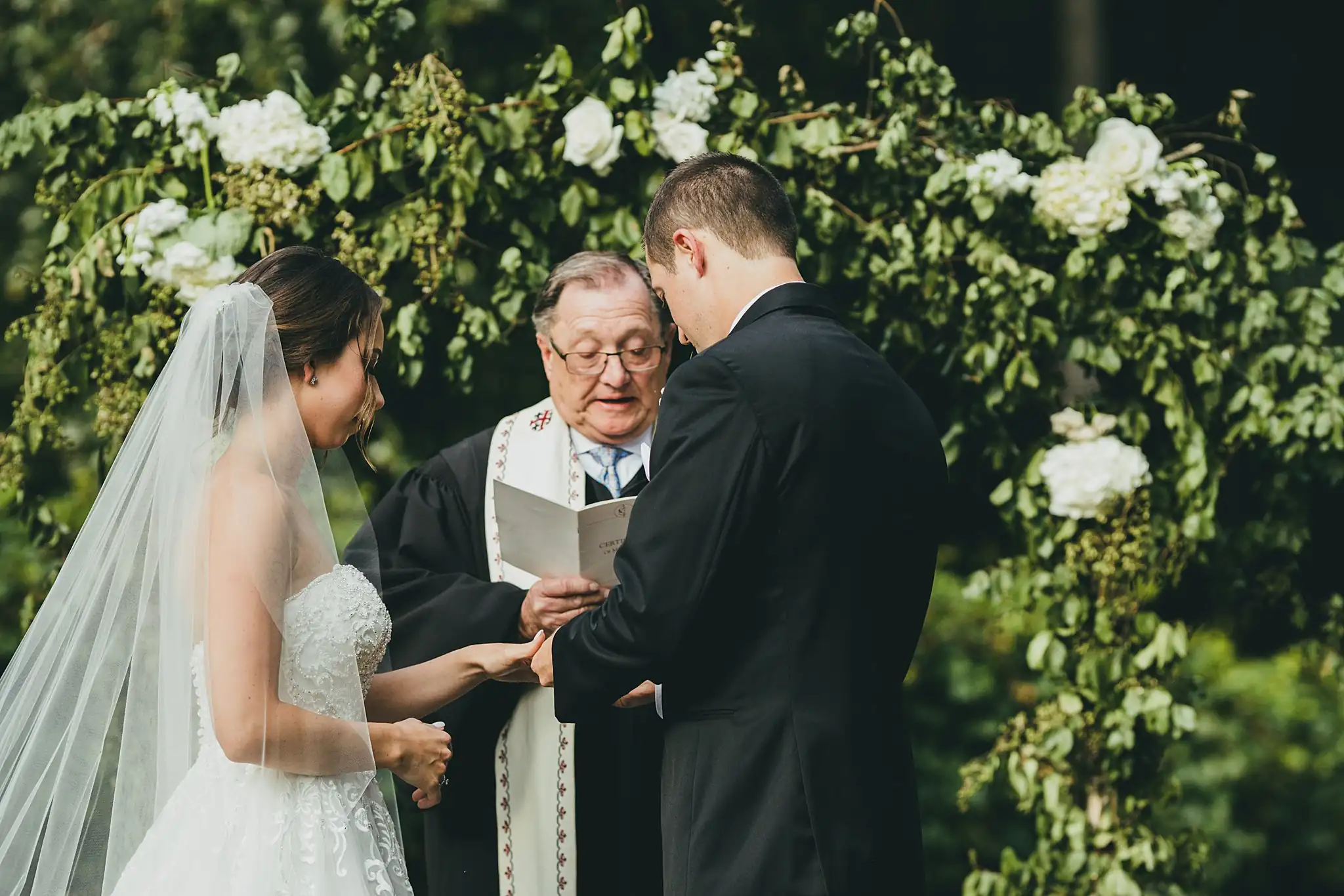 Wedding Ceremony: the officiant reading beneath the hydrangea arch, at their wedding at Little River Farms in Milton, GA