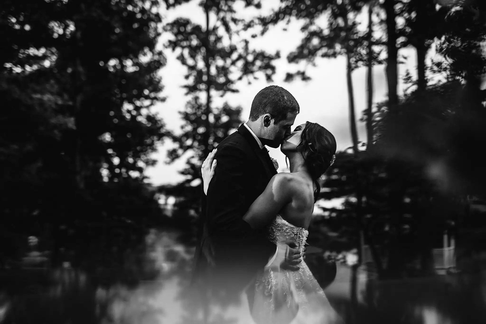 Wedding Formals: the couple kissing by the water, in black and white, at their wedding at Little River Farms in Milton, GA