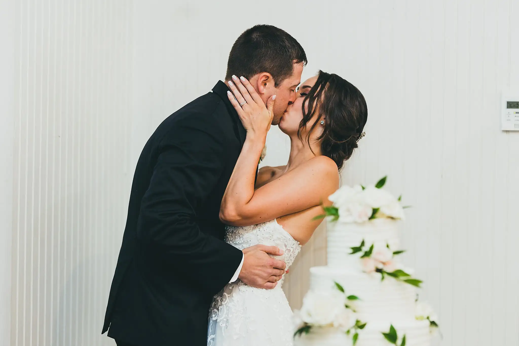 Cake Cutting: the couple kissing beside the cake, at their wedding at Little River Farms in Milton, GA