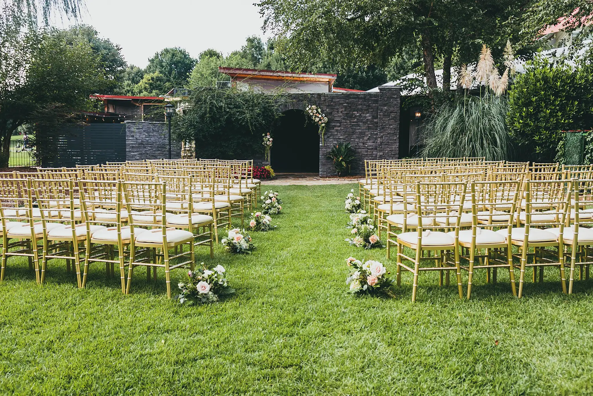 Wedding Ceremony: the lawn set with gold chairs at the stone wall, at a wedding at the Piedmont Garden Tent in Atlanta, GA