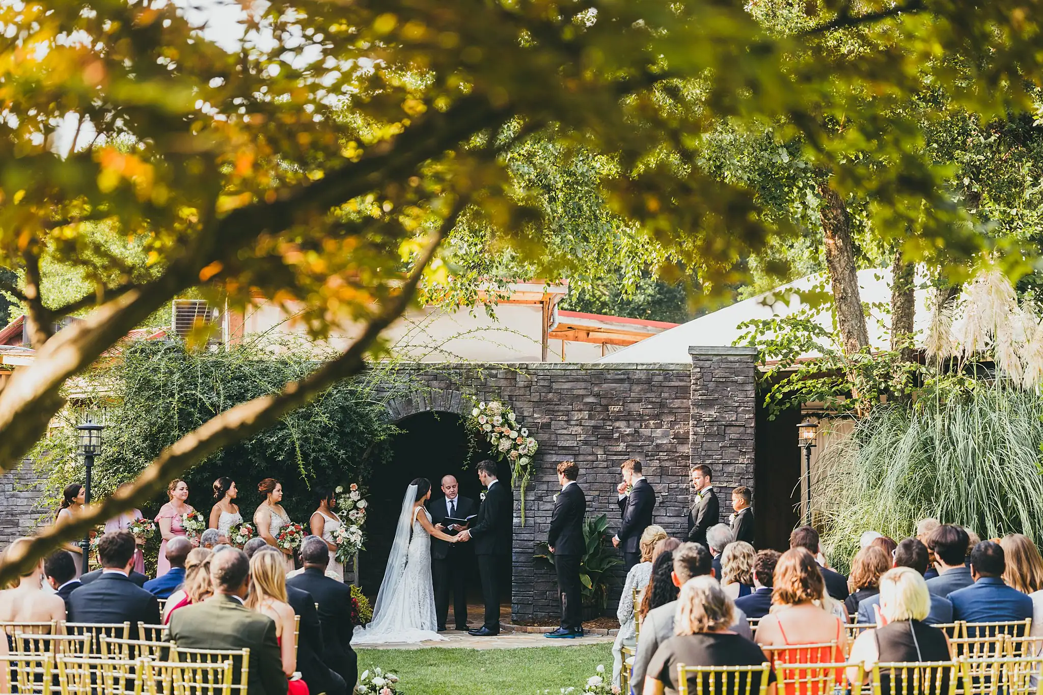 Wedding Ceremony: the ceremony framed by a tree, at their wedding at the Piedmont Garden Tent in Atlanta, GA