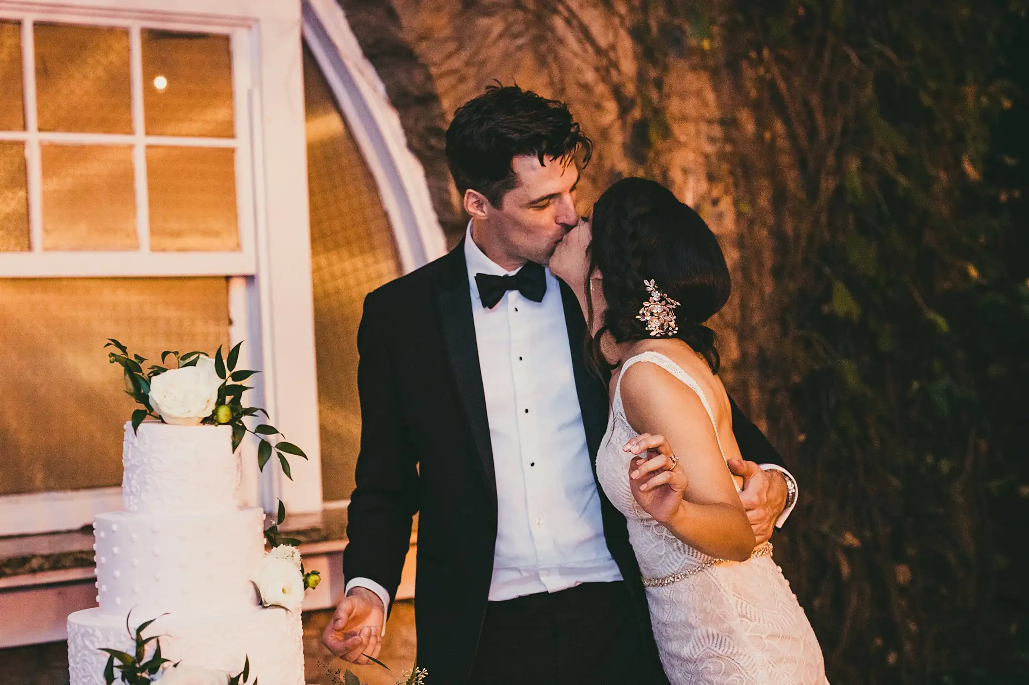 Cake Cutting: the couple kissing beside the cake, at their wedding at the Piedmont Garden Tent in Atlanta, GA