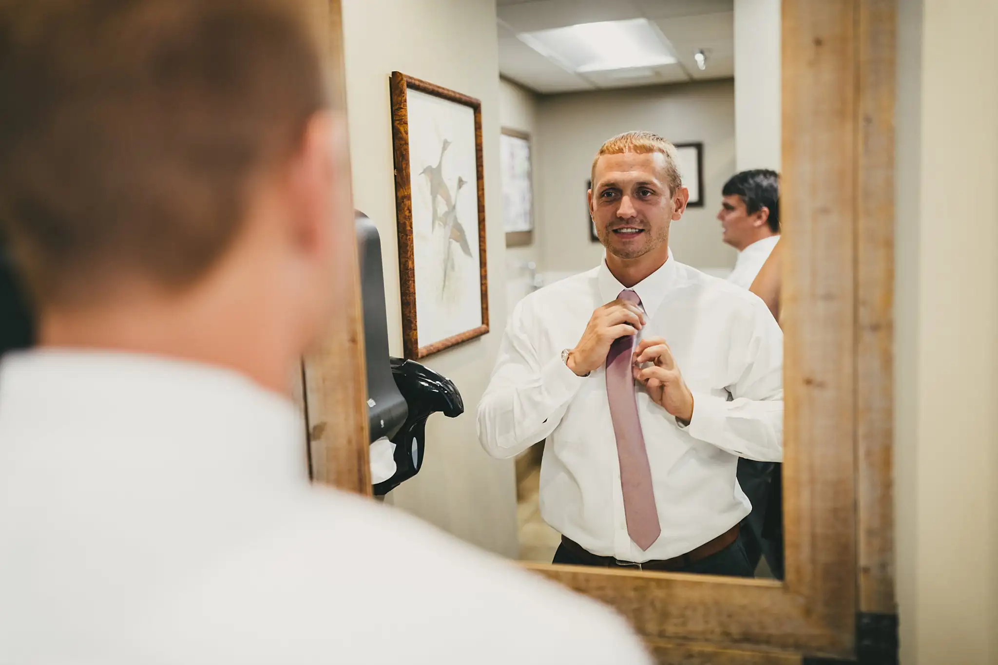 Getting Ready: the groom at the mirror with his tie, before their wedding at Houston Lake Country Club in Perry, GA