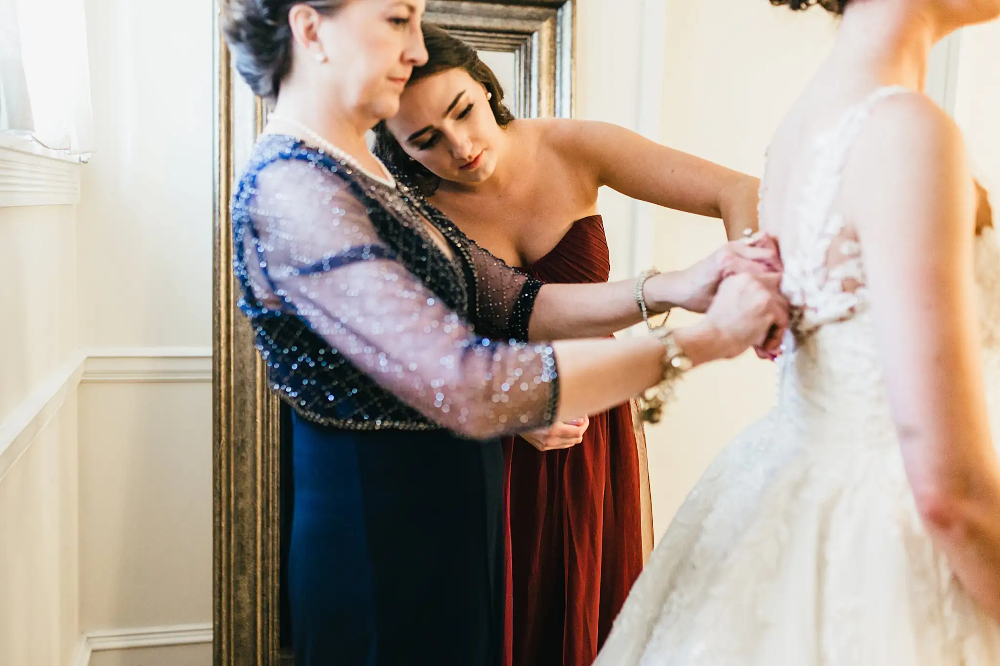 Getting Ready: a bridesmaid fastening the back of the gown, before their wedding at Ashton Gardens Atlanta in Sugar Hill, GA