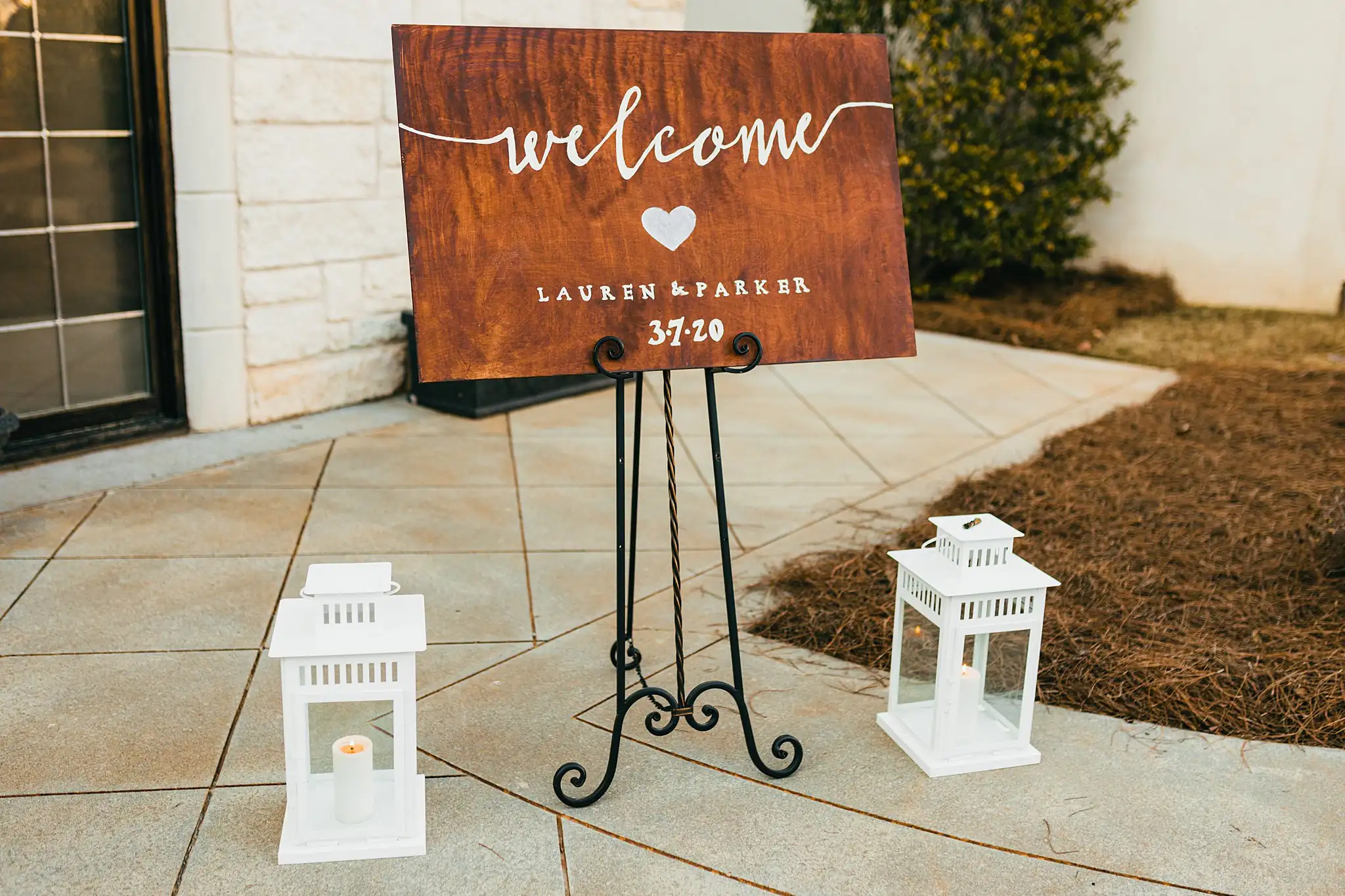 Wedding Details: a wooden welcome sign between white lanterns, at a wedding at Ashton Gardens Atlanta in Sugar Hill, GA