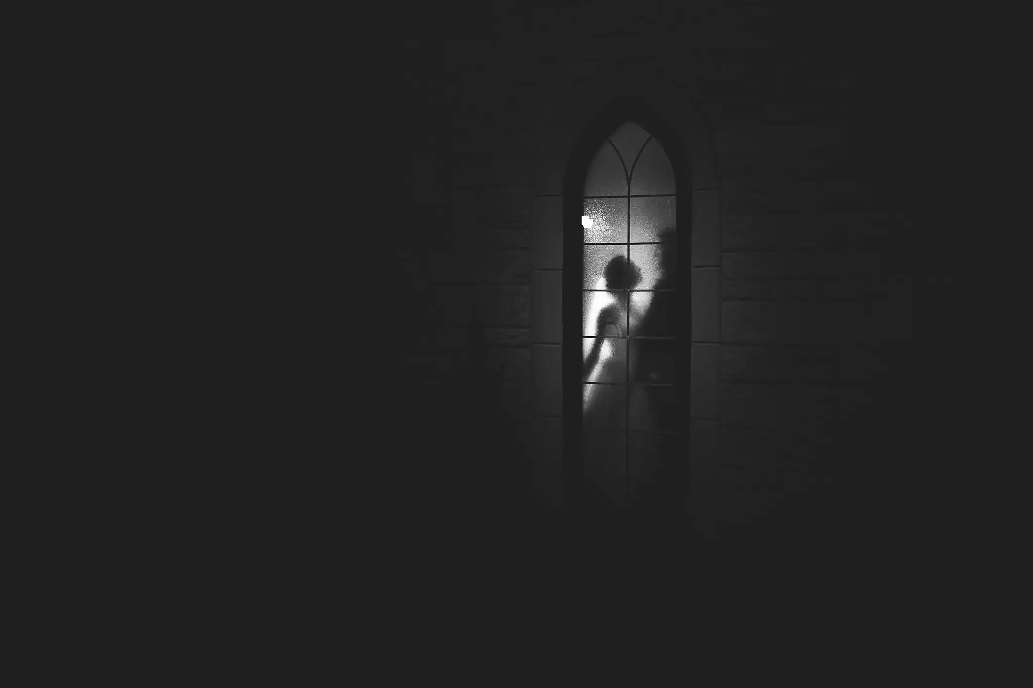 Wedding Ceremony: a lit arched window in the chapel's stone wall, at a wedding at Ashton Gardens Atlanta in Sugar Hill, GA