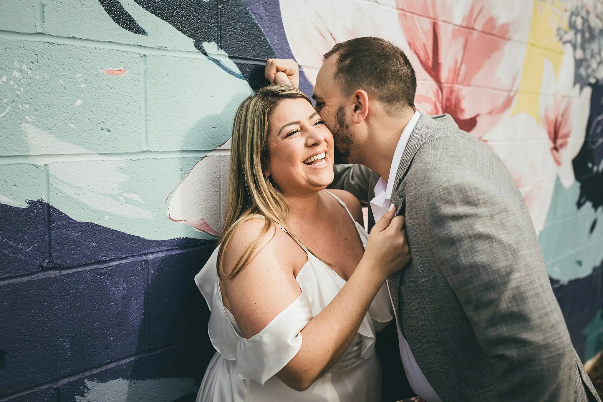 Engagement Portraits: him kissing her temple at the painted wall, during their engagement session at Marietta Square in Marietta, GA