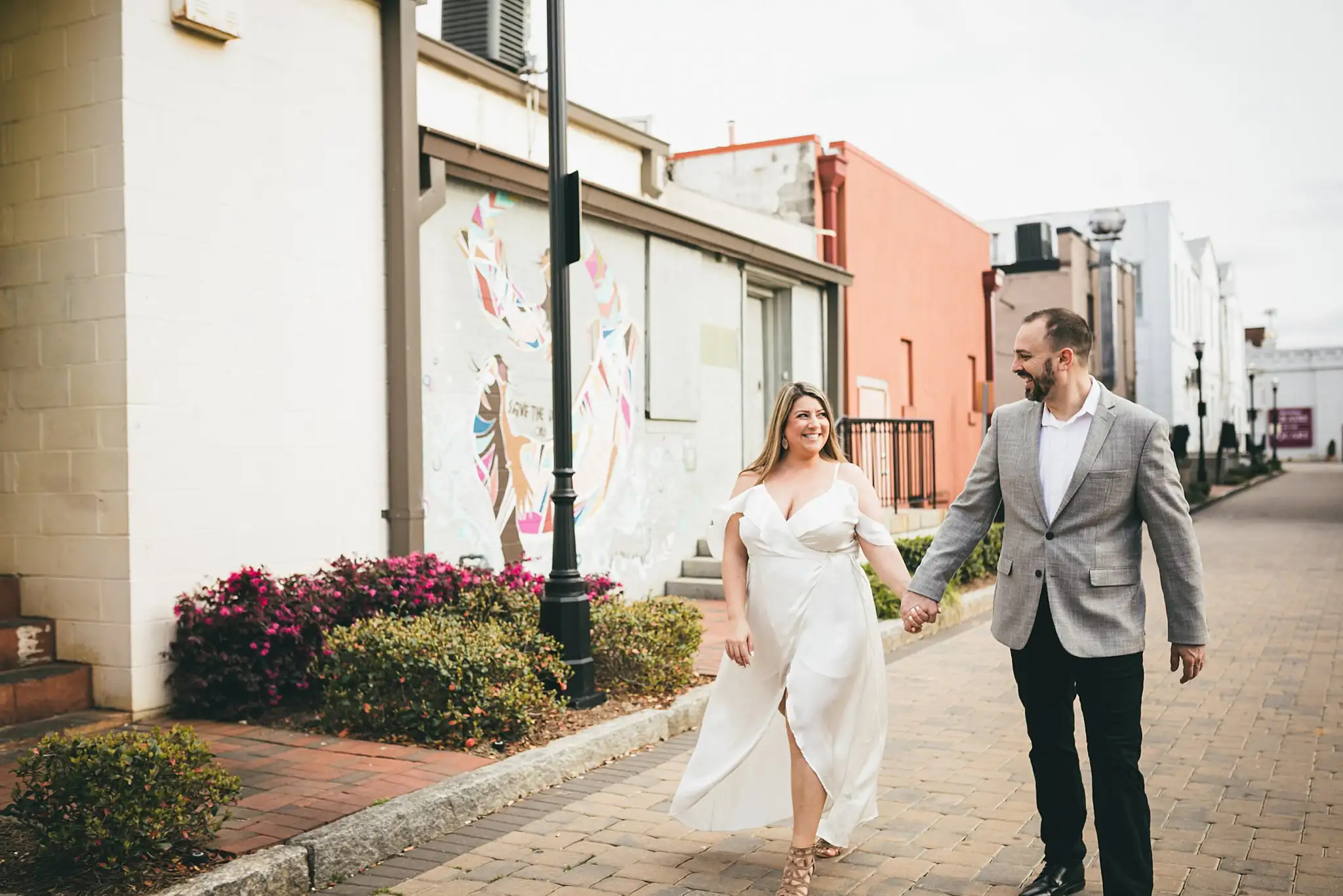 Engagement Portraits: walking the sidewalk past the storefronts, during their engagement session at Marietta Square in Marietta, GA