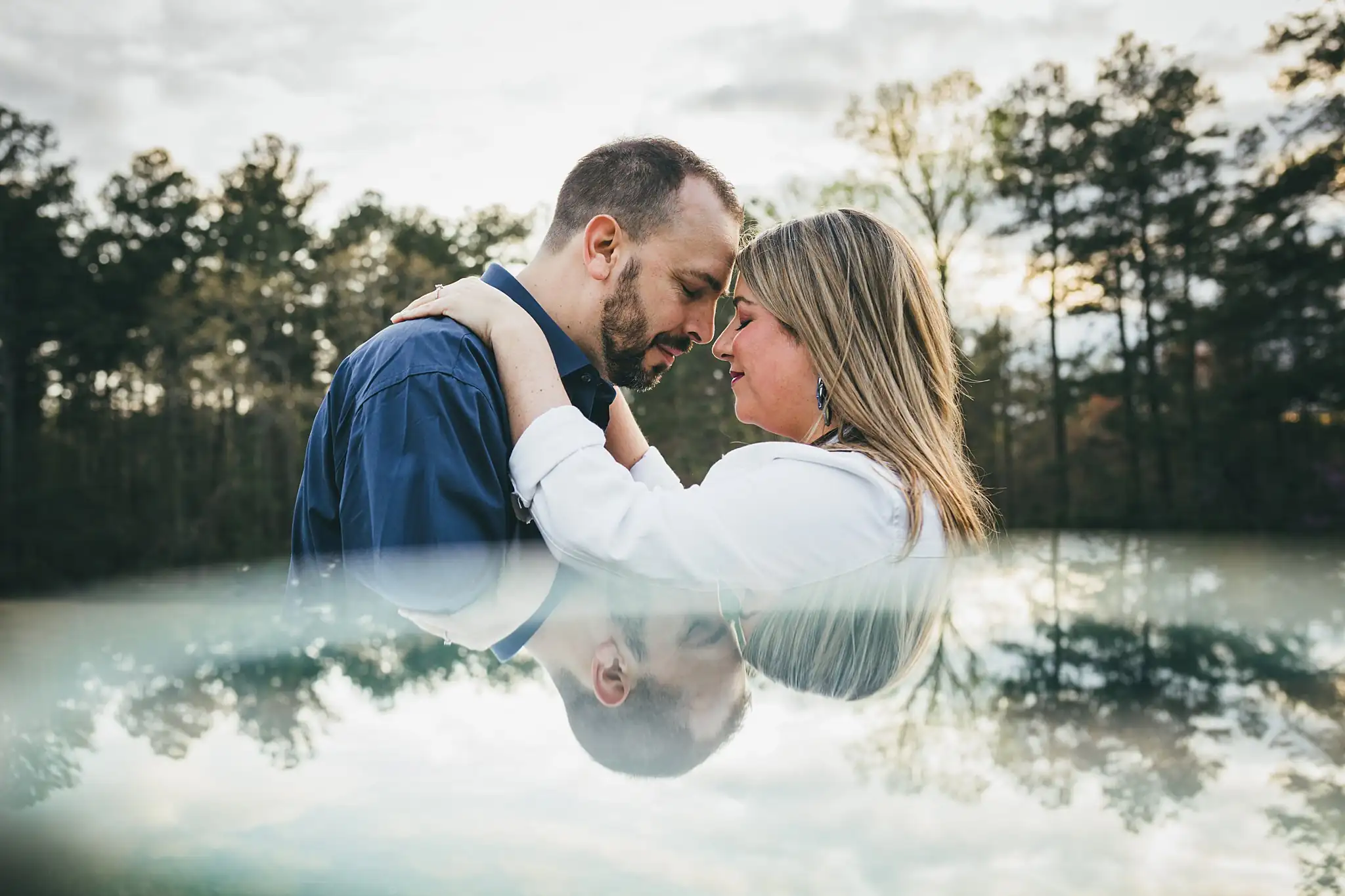 Engagement Portraits: foreheads together above their reflection in the pond, during their engagement session at Kennesaw Mountain in Kennesaw, GA