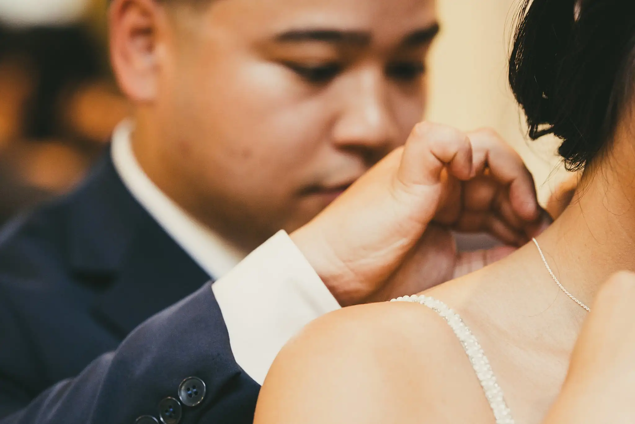 Getting Ready: the groom fastening the bride's necklace, before their wedding at the Atlanta Botanical Garden in Atlanta, GA