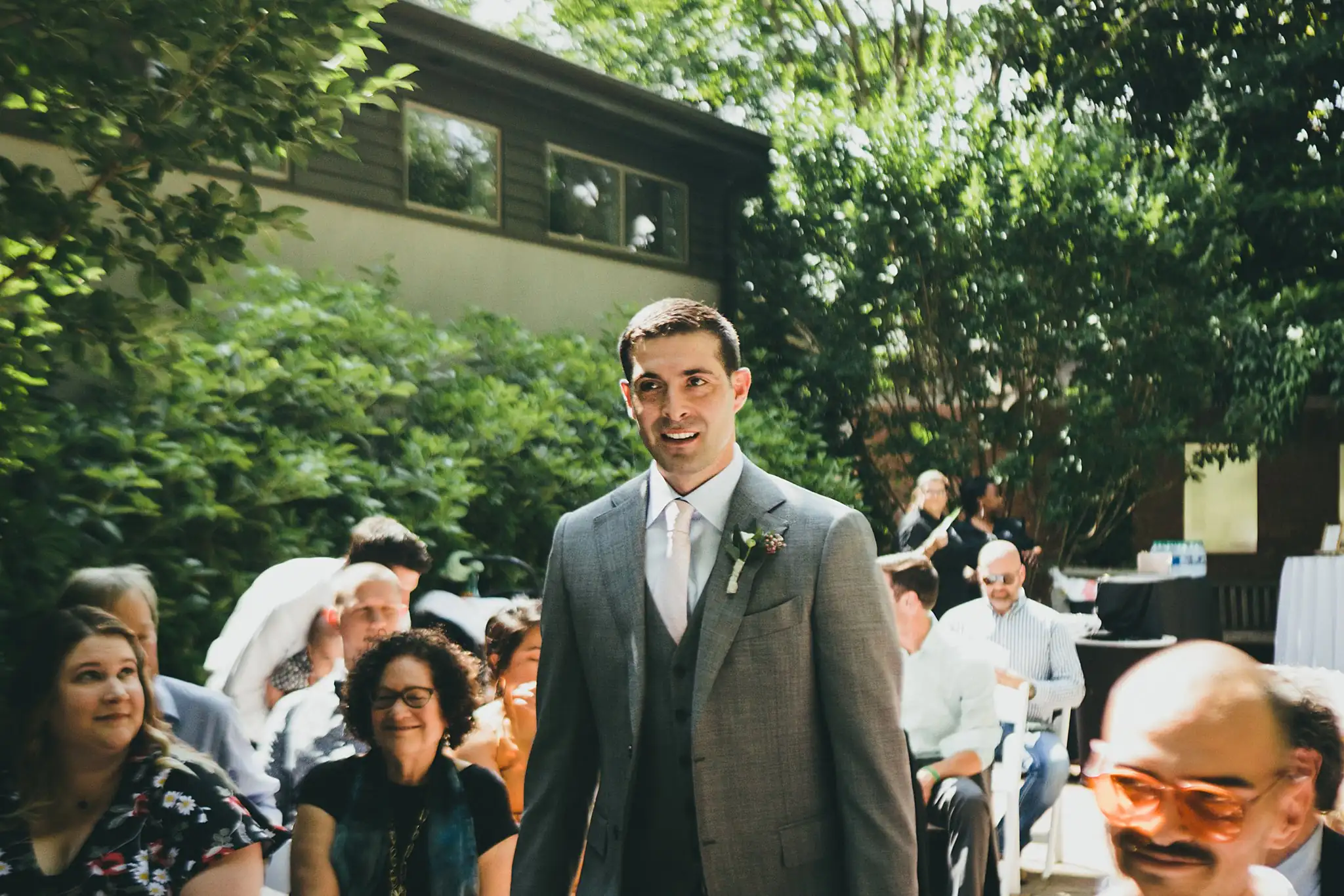 Processional: the groom walking in past the seated guests, at their wedding at the Atlanta Botanical Garden in Atlanta, GA