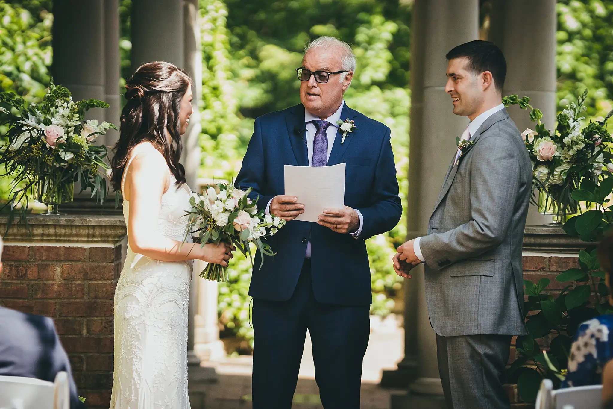 Wedding Ceremony: the couple with the officiant at the brick wall, at their wedding at the Atlanta Botanical Garden in Atlanta, GA
