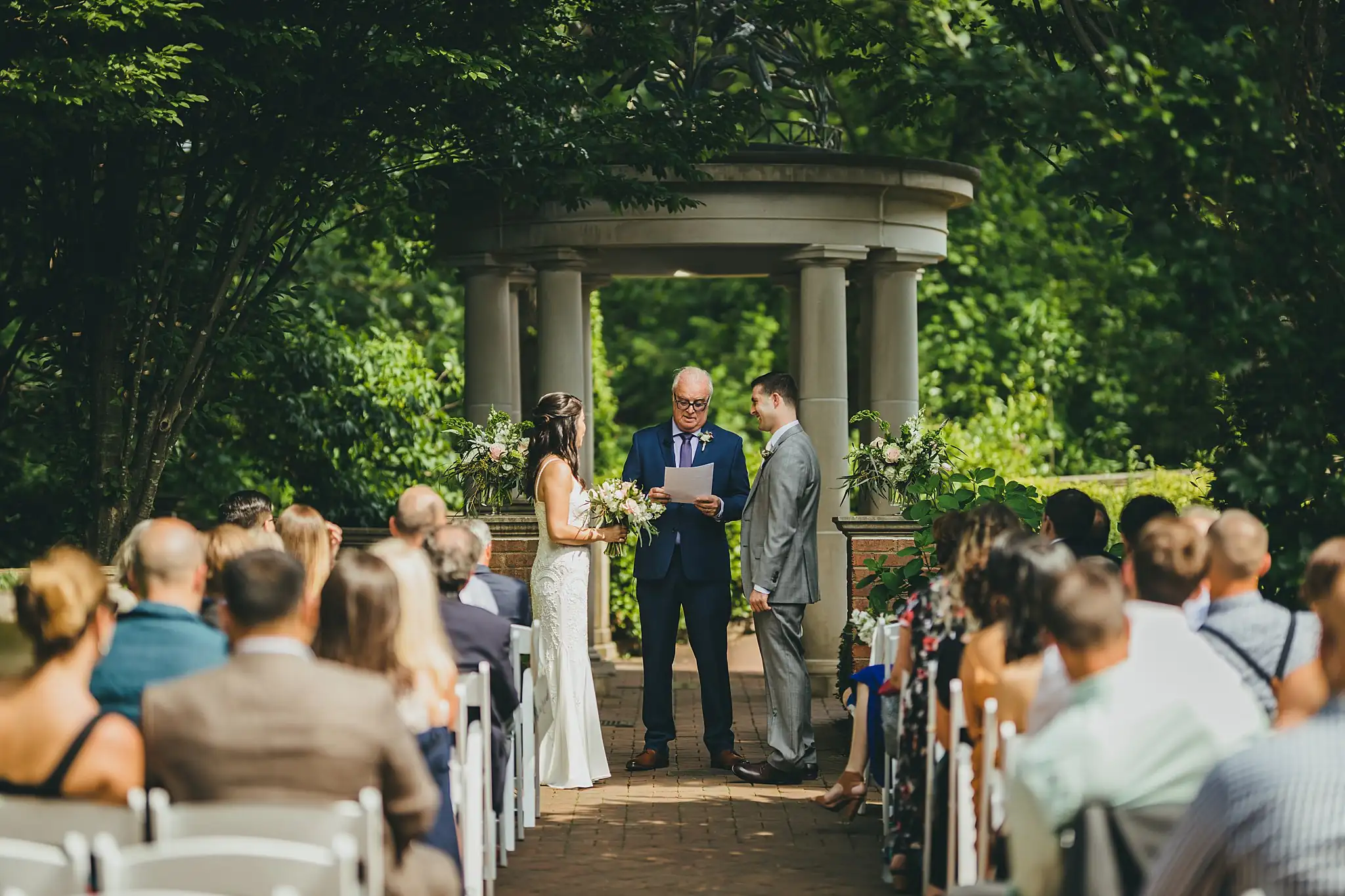 Wedding Ceremony: the couple at the pavilion, seen up the aisle, at their wedding at the Atlanta Botanical Garden in Atlanta, GA