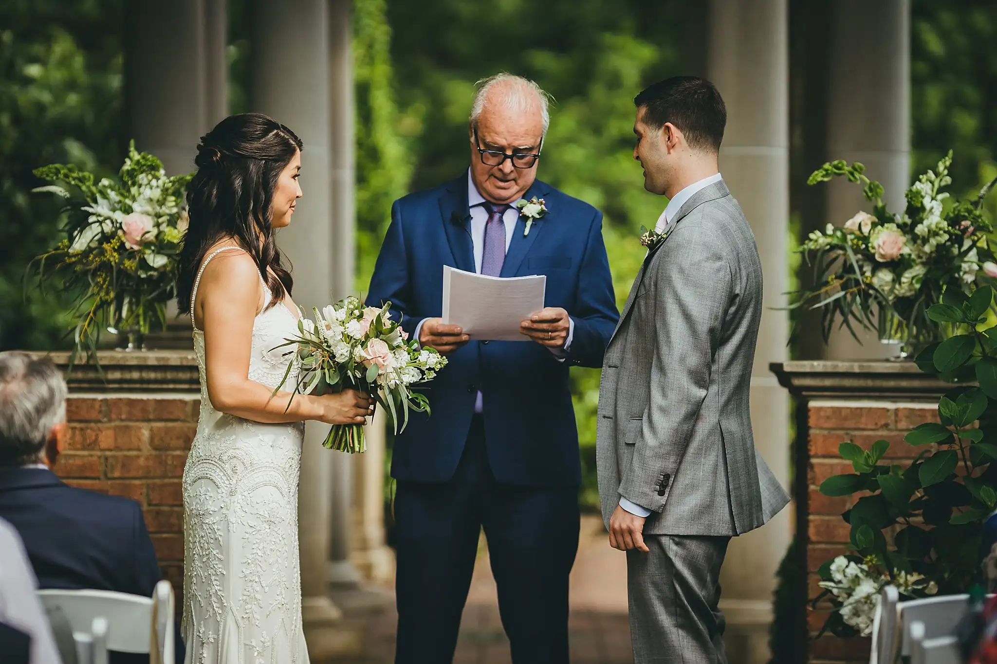Wedding Ceremony: the officiant reading, florals either side, at their wedding at the Atlanta Botanical Garden in Atlanta, GA