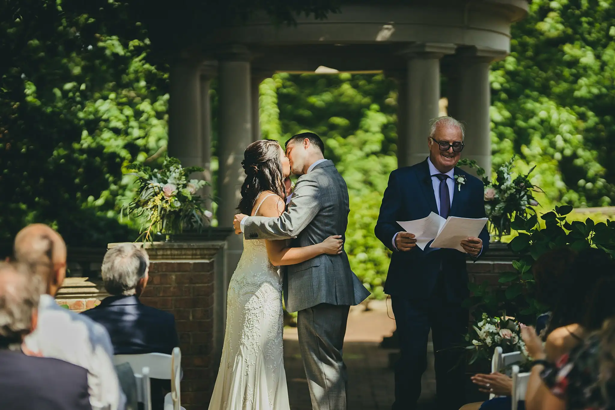 Wedding Ceremony: the first kiss beneath the colonnade, at their wedding at the Atlanta Botanical Garden in Atlanta, GA