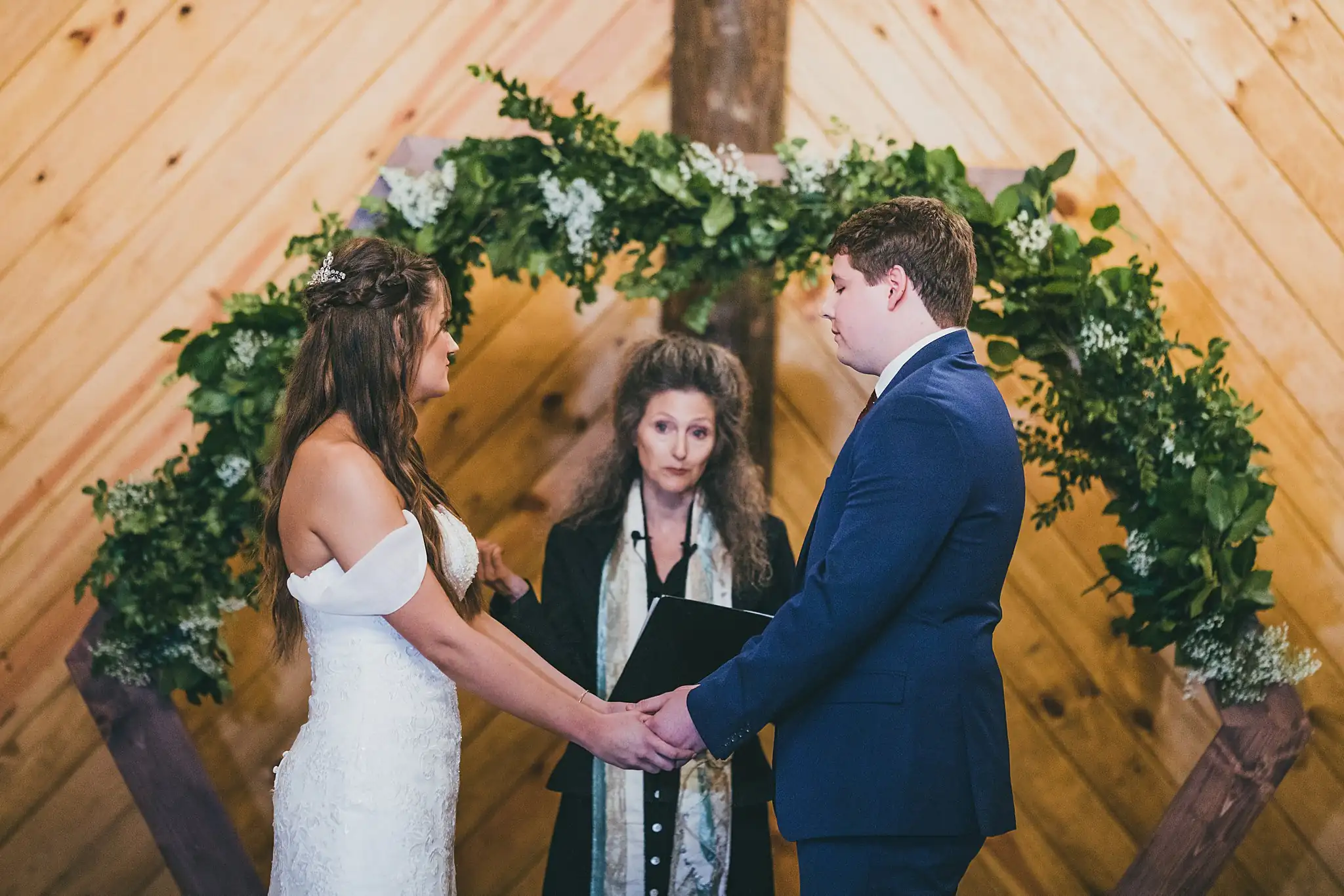 Barn at Harper Pines Wedding Thomaston, GA Atlanta Wedding Photographers Wedding Ceremony: the couple holding hands beneath the greenery arch, at their wedding at the Barn at Harper Pines in Thomaston, GA