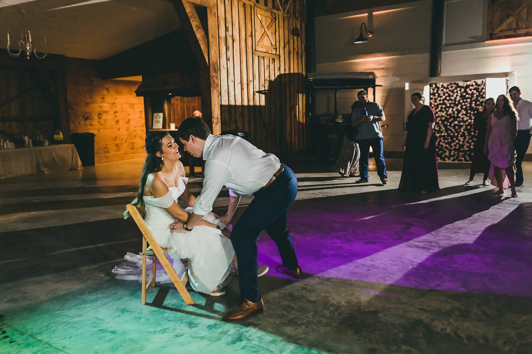 Barn at Harper Pines Wedding Thomaston, GA Atlanta Wedding Photographers Garter Toss: the groom removing the bride's garter, at their wedding at the Barn at Harper Pines in Thomaston, GA