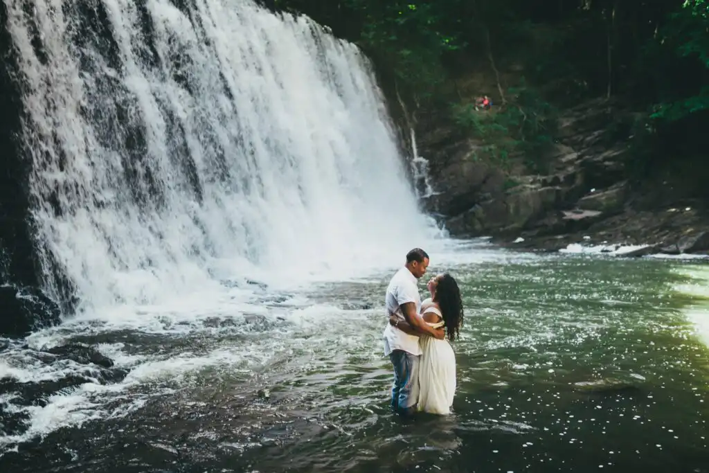 Engagement Portraits: a couple standing waist-deep in the pool below Vickery Creek Falls, during their engagement session in Roswell, GA