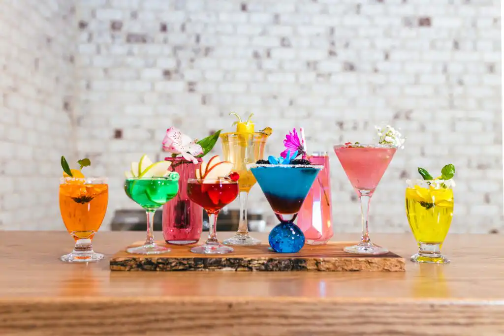 Reception Details: eight brightly colored cocktails lined up on a wooden board, at the Whimsically in Love styled wedding shoot at Brick and Ivey Event Venue in Atlanta, GA