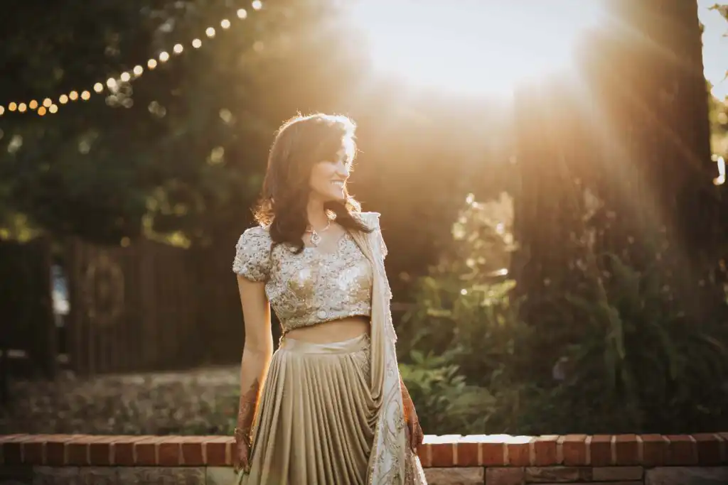 Bridal Portraits: the bride in a gold lehenga with mehndi on her hands, backlit by the setting sun on her wedding day