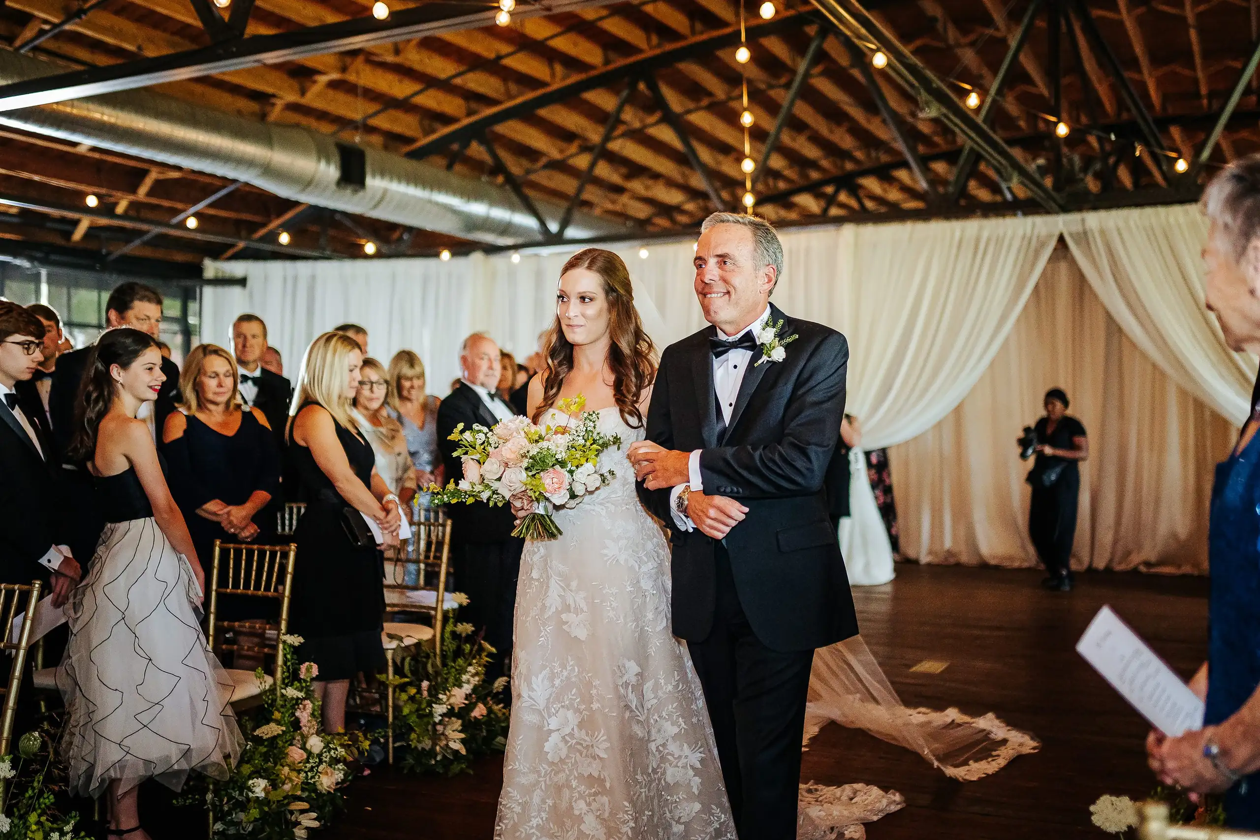 Processional: the bride coming down the aisle on her father's arm, at their wedding at Summerour Studio in Atlanta, GA