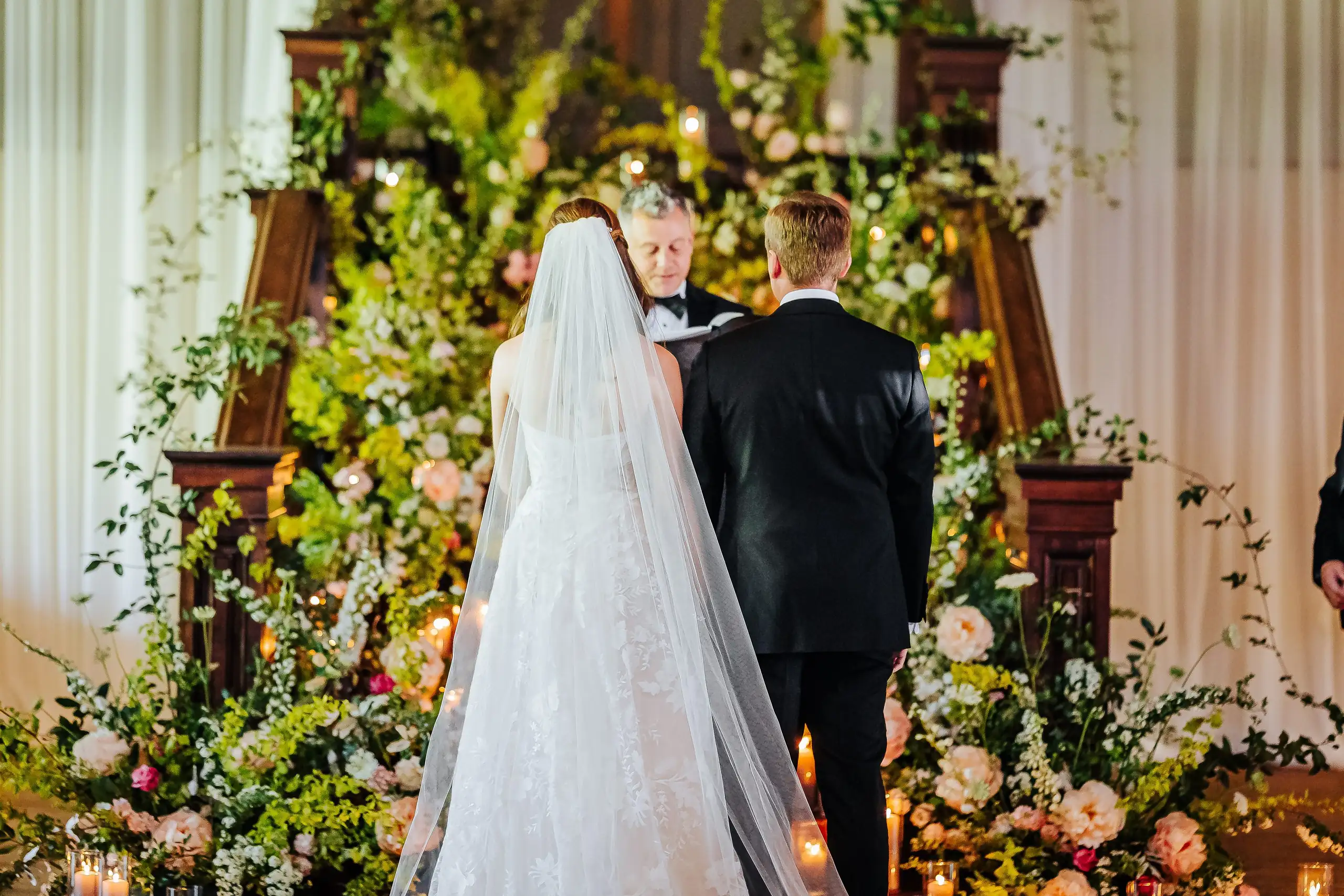 Wedding Ceremony: the couple facing each other at the flower-banked altar, at their wedding at Summerour Studio in Atlanta, GA