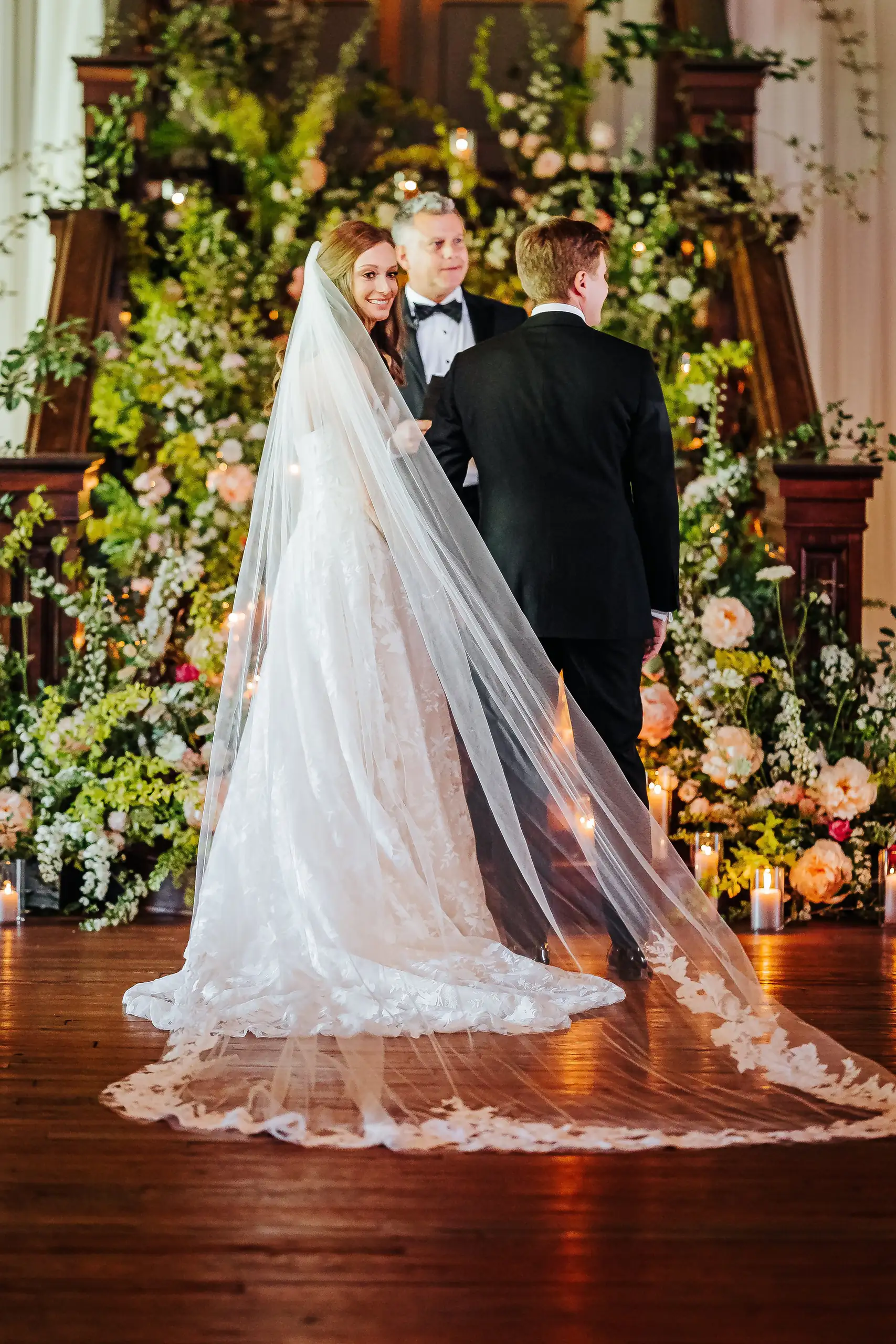 Wedding Ceremony: the couple at the floral altar with the veil spread behind, at their wedding at Summerour Studio in Atlanta, GA