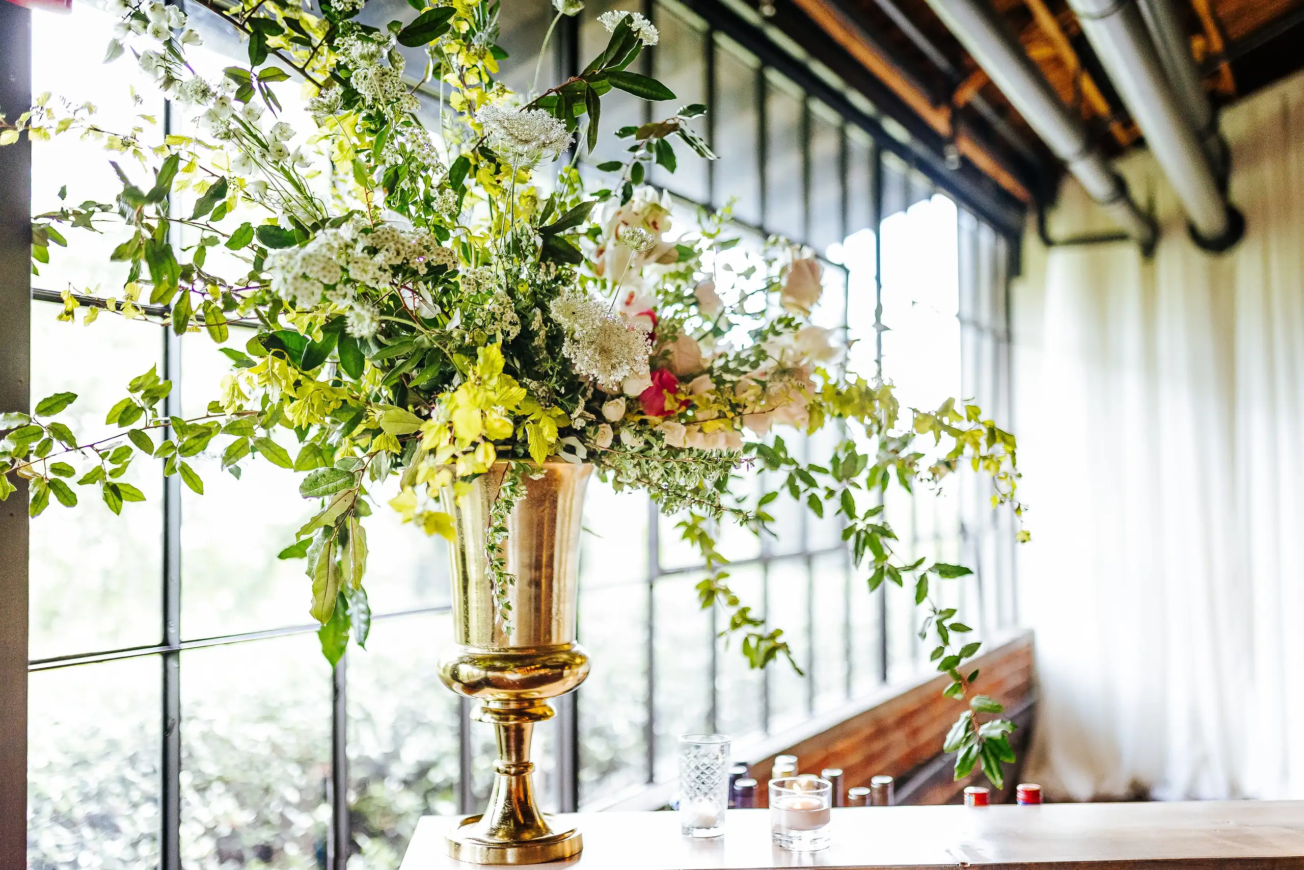 Reception Details: a tall gold urn arrangement against the windows, at a wedding at Summerour Studio in Atlanta, GA