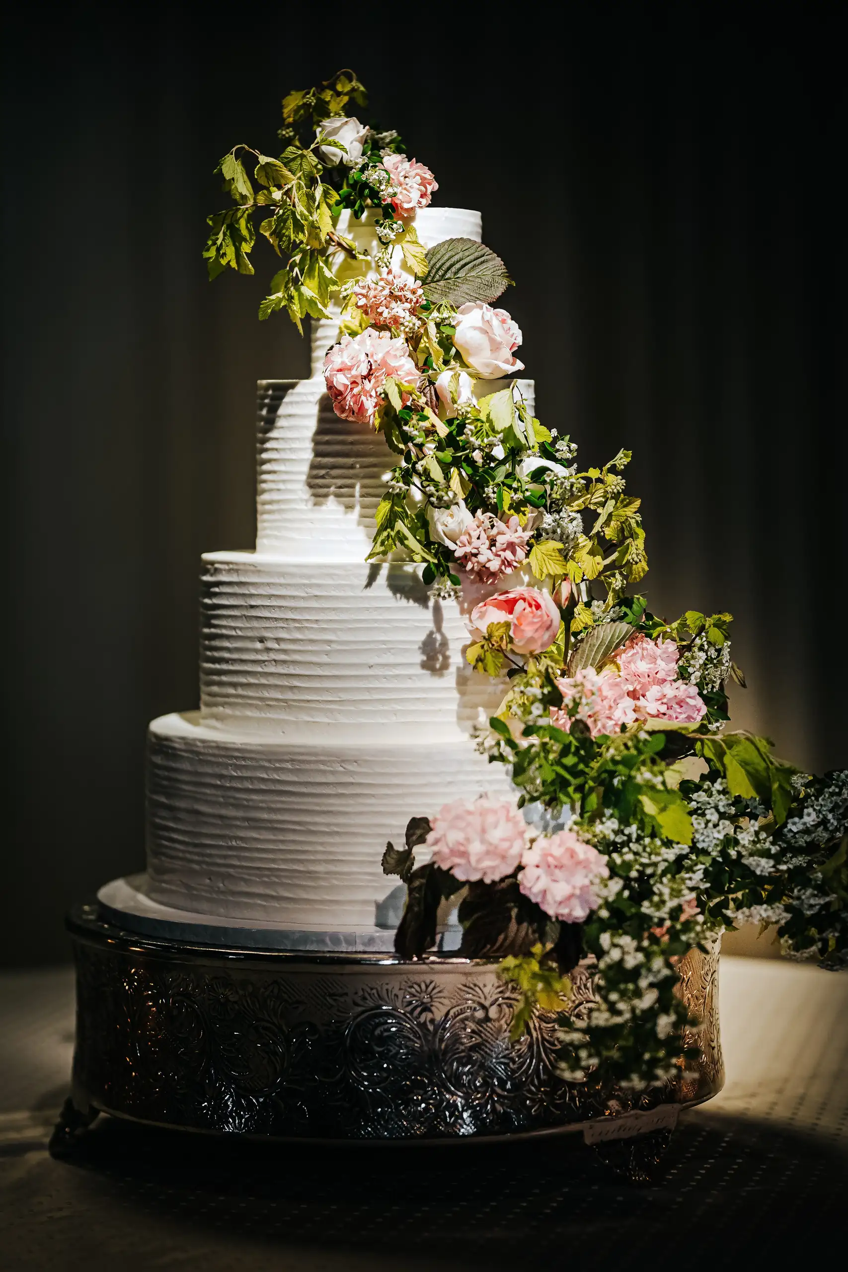 Wedding Cake Details: the tiered cake trimmed with flowers up one side, at a wedding at Summerour Studio in Atlanta, GA