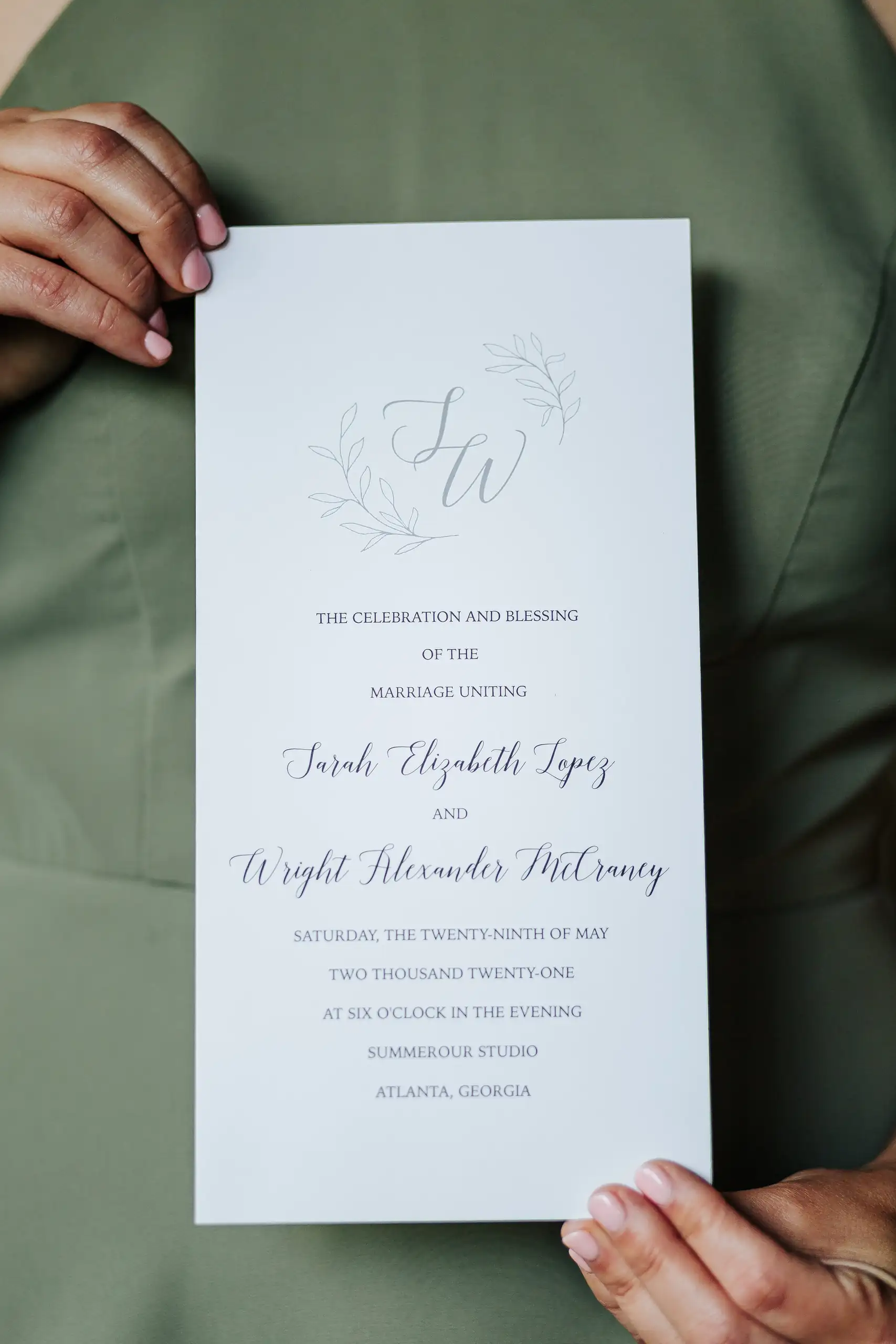 Wedding Details: the ceremony program held against a sage dress, at a wedding at Summerour Studio in Atlanta, GA