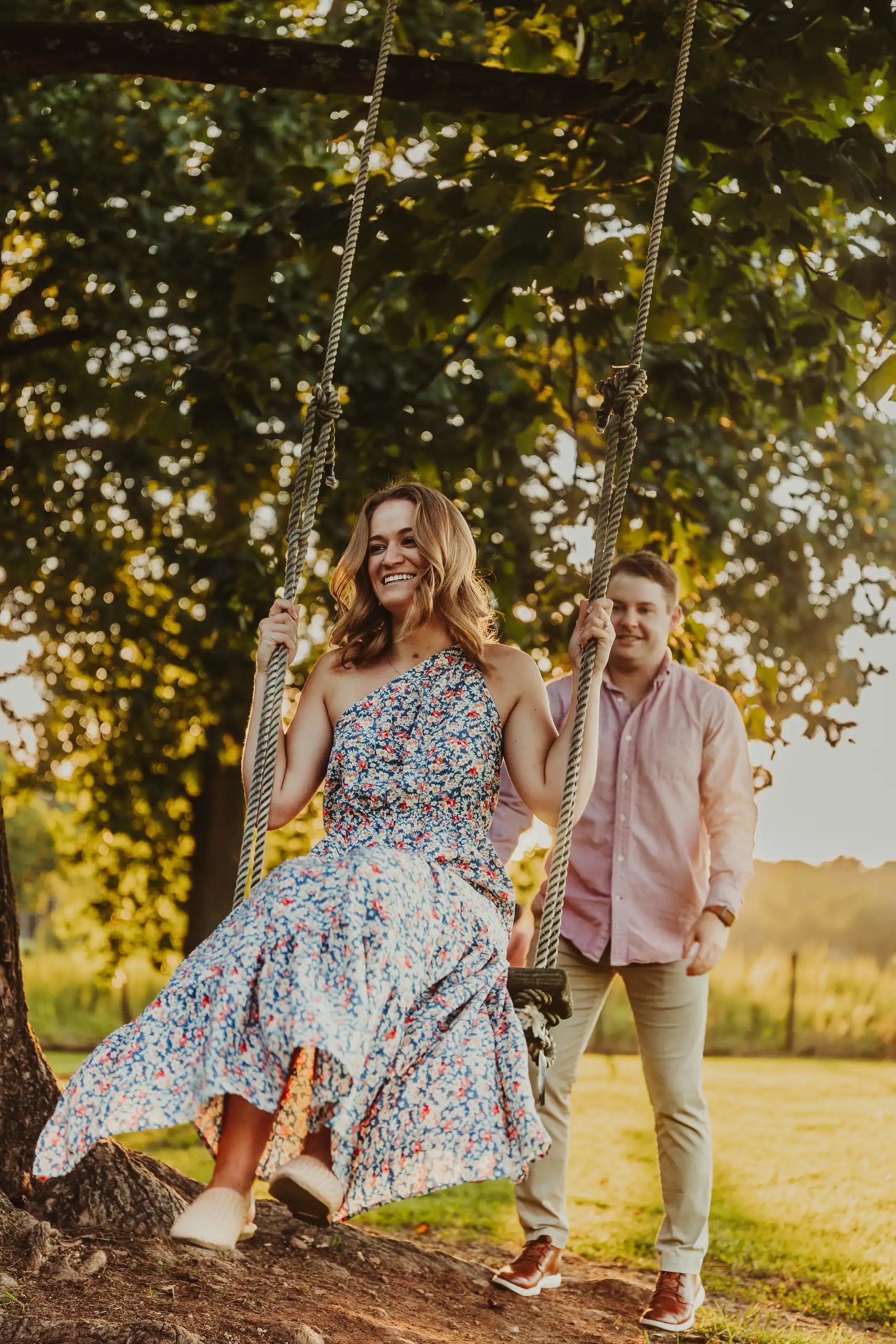 Engagement Portraits: him pushing the swing, both of them laughing, during their engagement session at Prospect Farms in Lawrenceville, GA