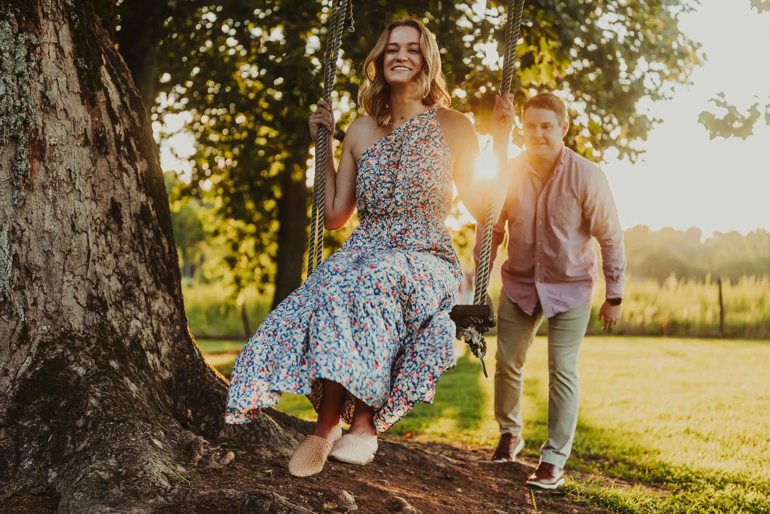 Engagement Portraits: her on the tree swing as he watches, during their engagement session at Prospect Farms in Lawrenceville, GA