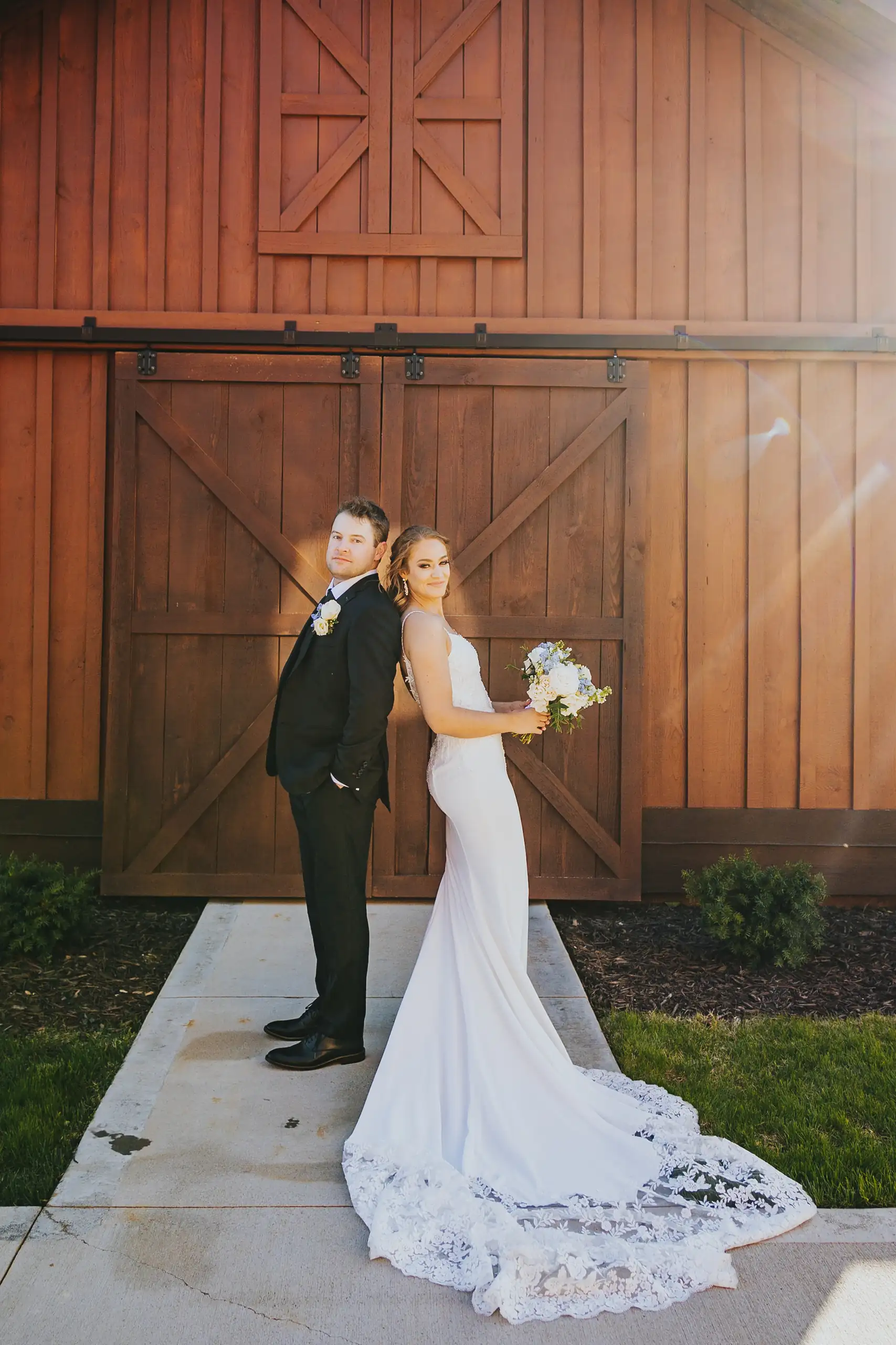 Wedding Formals: the couple by the barn, her train spread, at their wedding at The Venue at Sharp Mountain in Jasper, GA