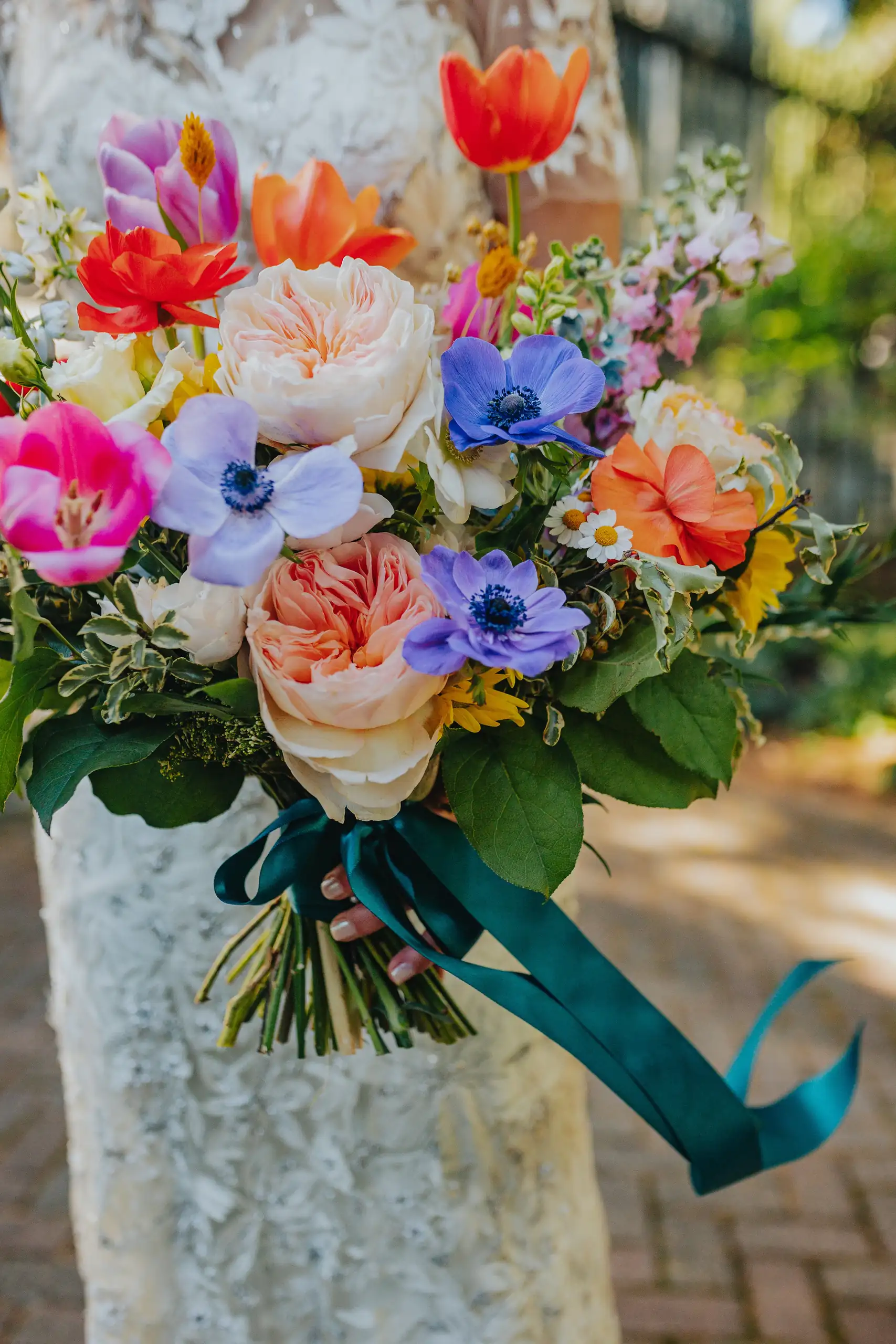 Wedding Florals: the bright bouquet held against a stone column, at a wedding at the Trolley Barn in Atlanta, GA