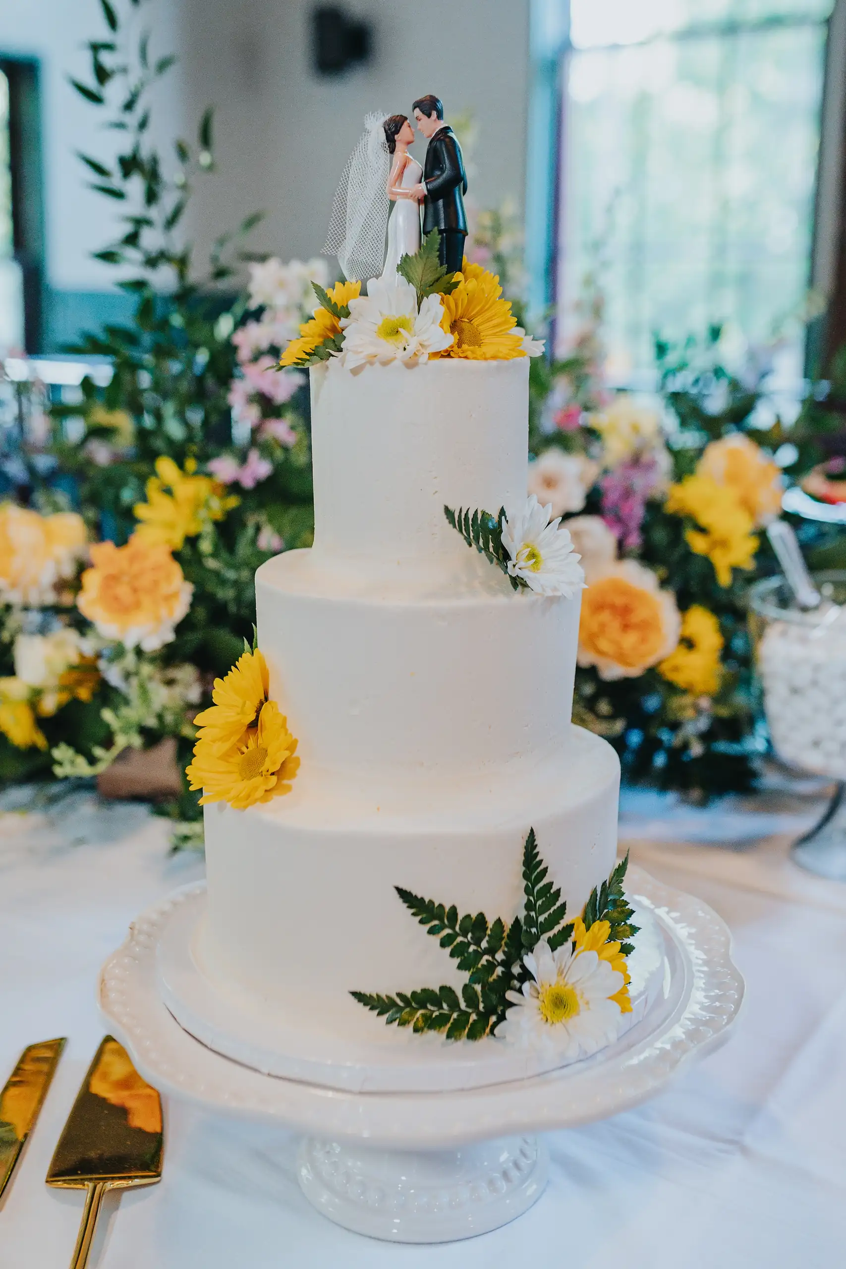 Wedding Cake Details: the tiered cake trimmed with yellow flowers and ferns, at their wedding at the Trolley Barn in Atlanta, GA