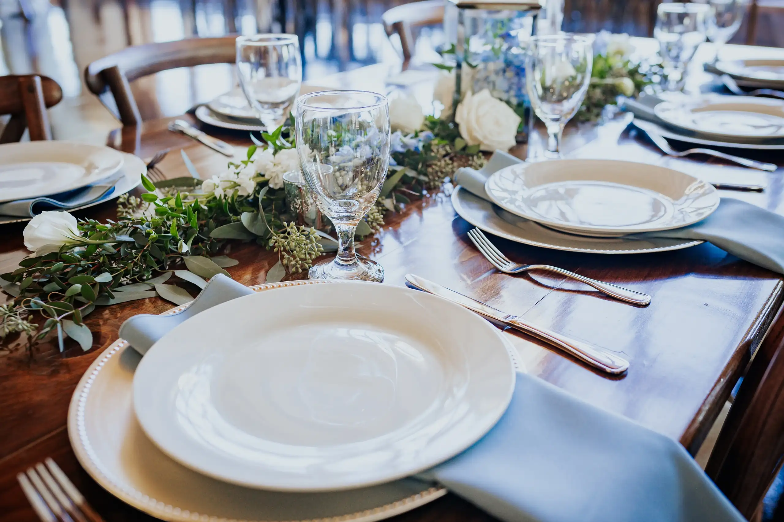 Reception Details: a place setting with a blue napkin and greenery, at their wedding at The Venue at Sharp Mountain in Jasper, GA
