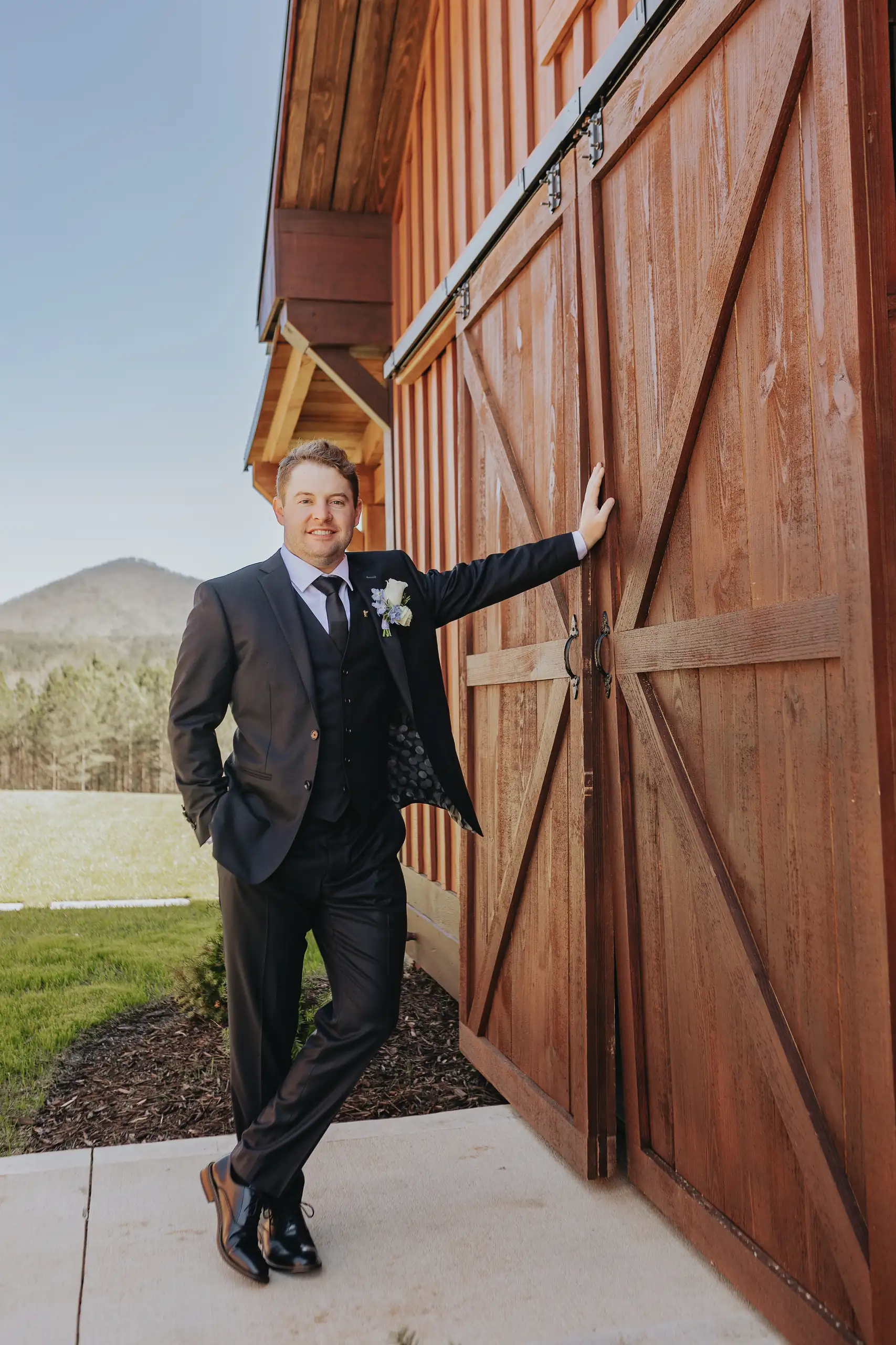 Wedding Formals: the groom leaning on the barn door, at their wedding at The Venue at Sharp Mountain in Jasper, GA