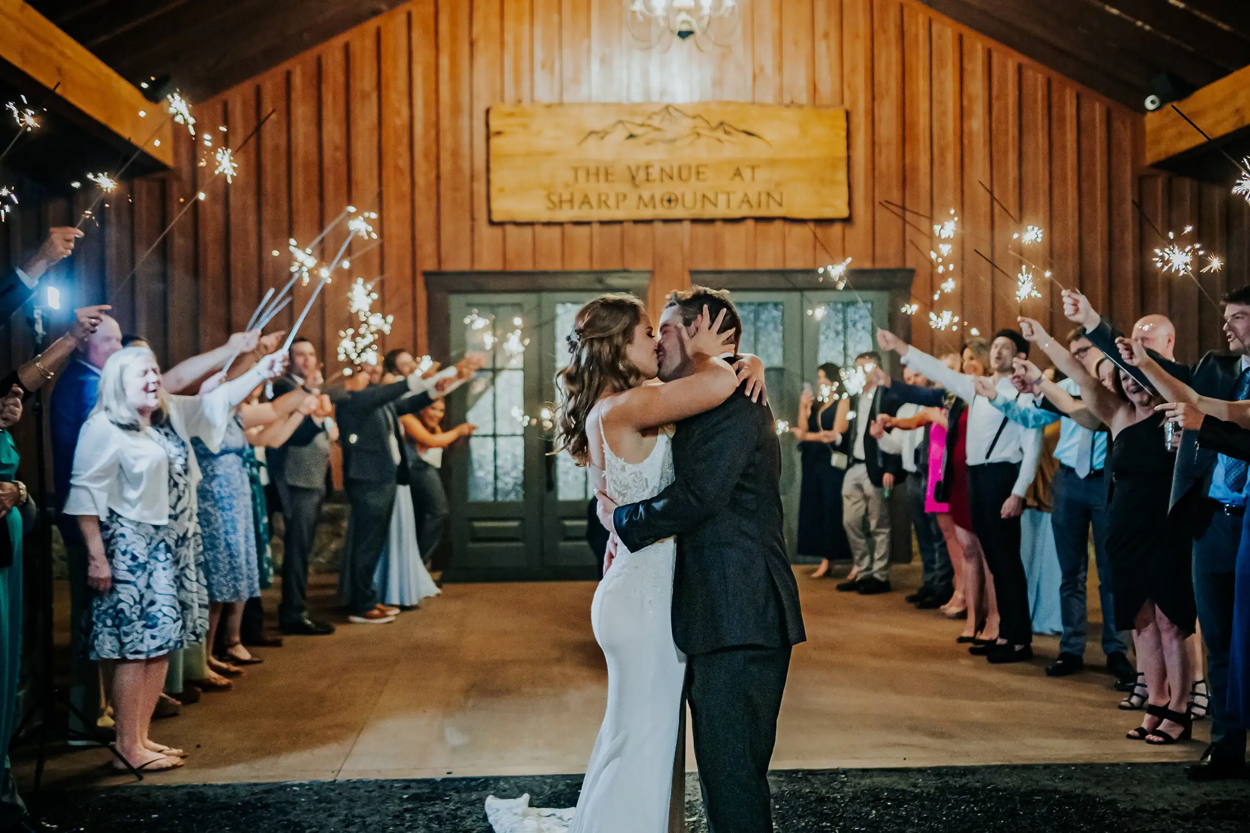 Sparkler Exit: the couple kissing beneath the carved venue sign, at their wedding at The Venue at Sharp Mountain in Jasper, GA
