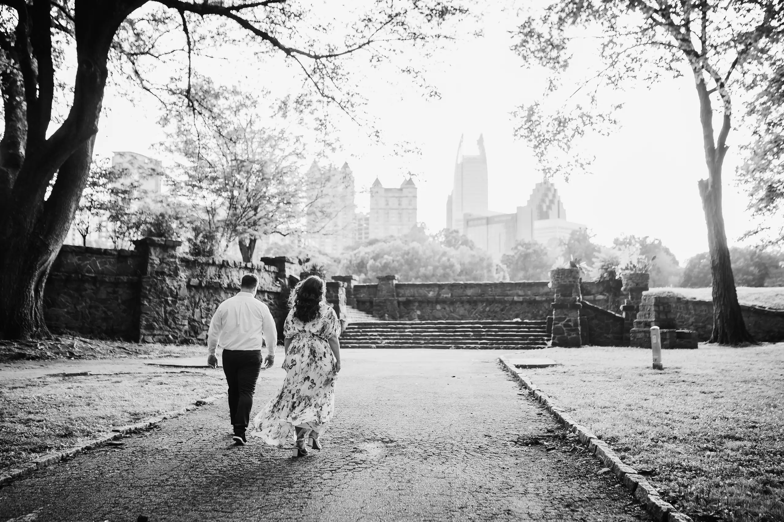 Engagement Portraits: walking the park path toward the skyline, in black and white, during their engagement session at Piedmont Park in Atlanta, GA