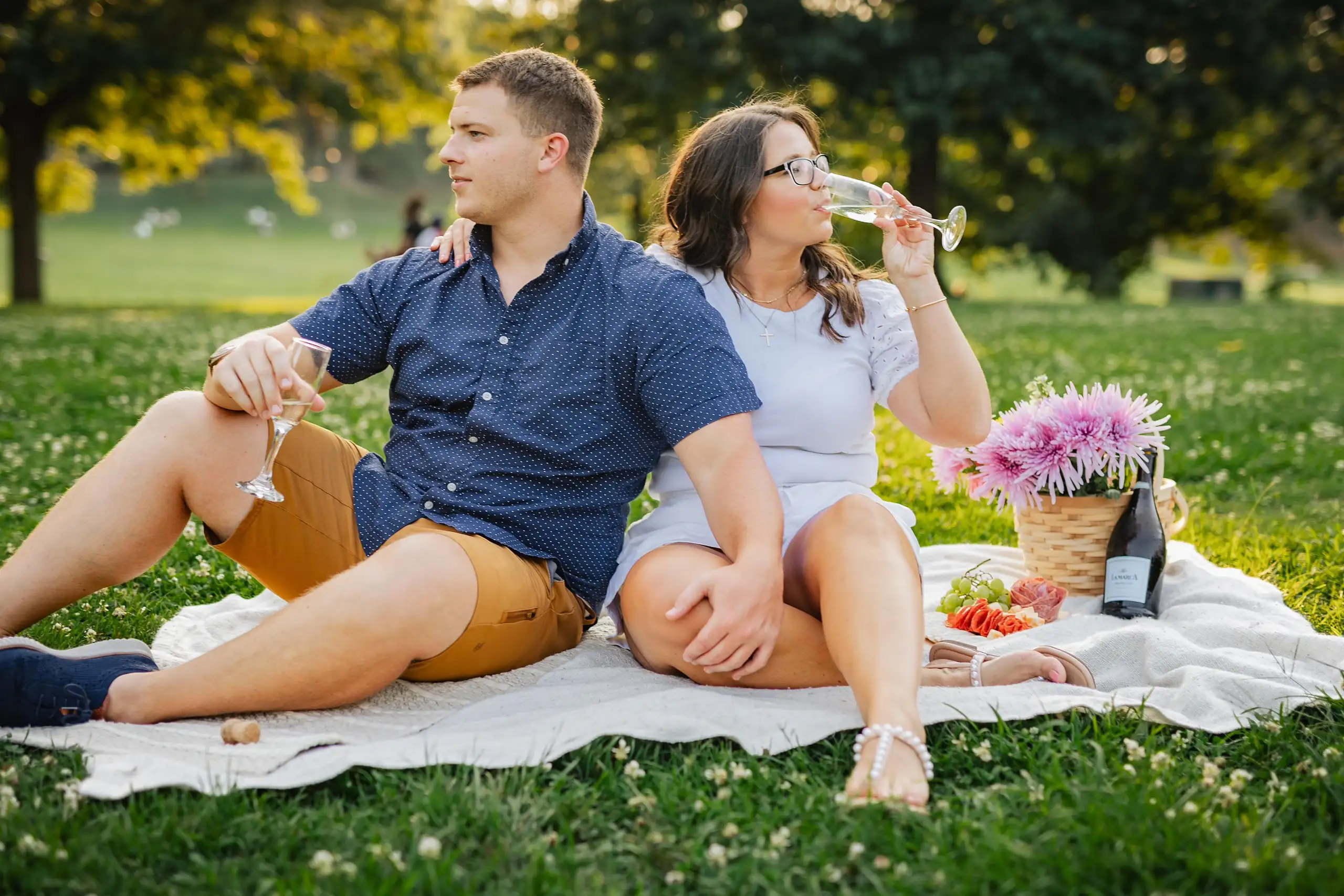 Engagement Portraits: a picnic on the grass with wine and a flower basket, during their engagement session