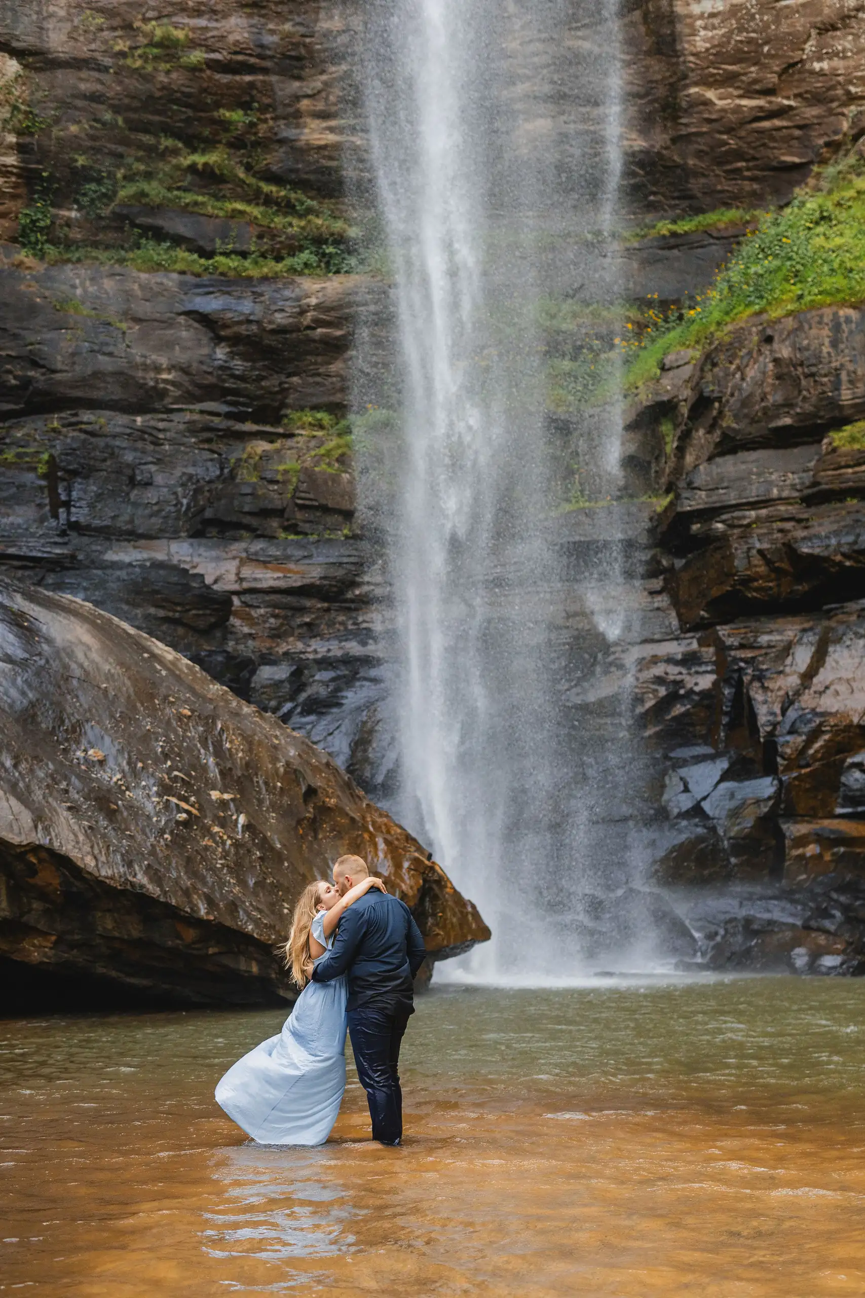 Engagement Portraits: a kiss standing in the pool at the foot of the drop, during their engagement session at Toccoa Falls in Toccoa, GA