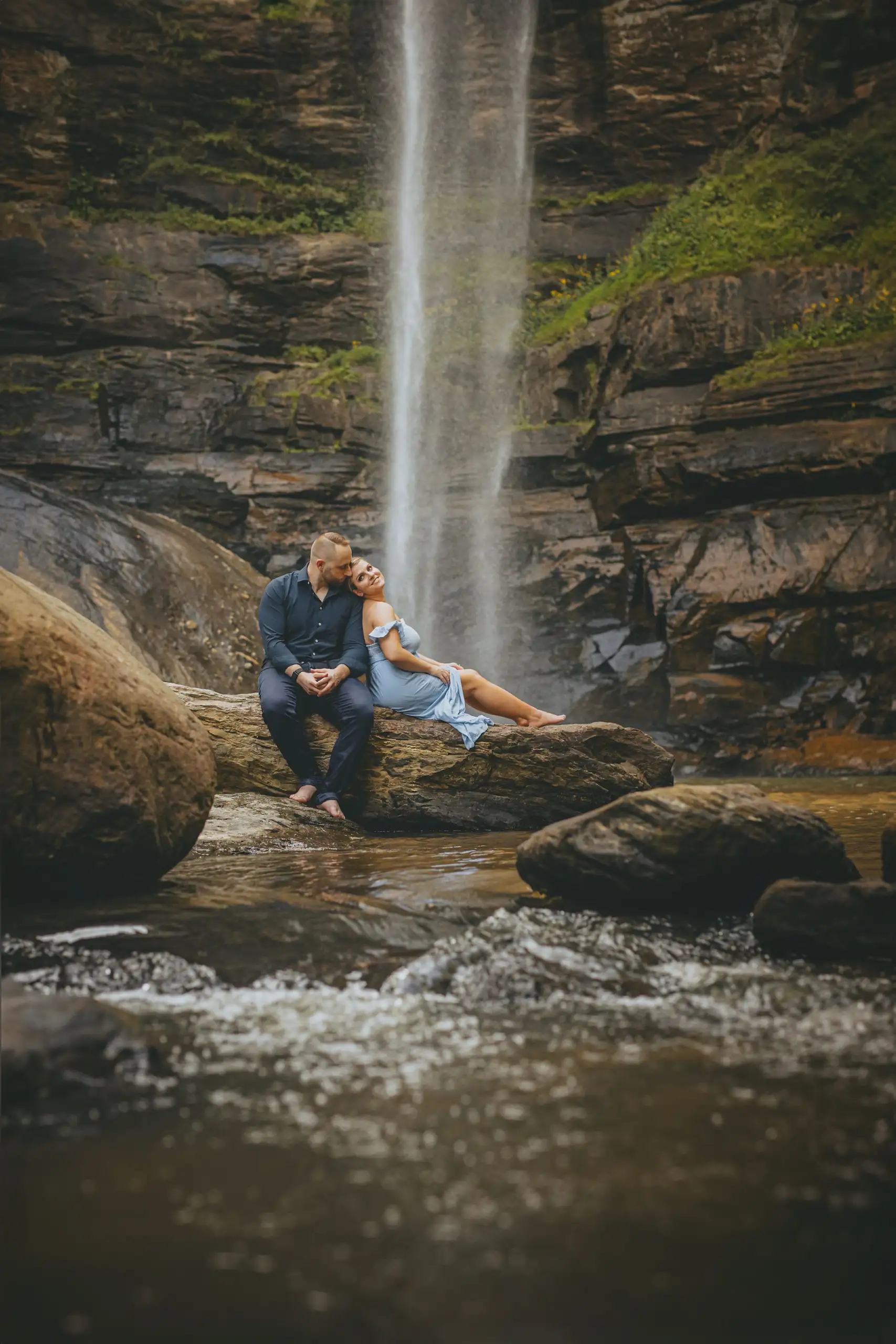 Engagement Portraits: the couple on the rocks with the water pouring behind, during their engagement session at Toccoa Falls in Toccoa, GA