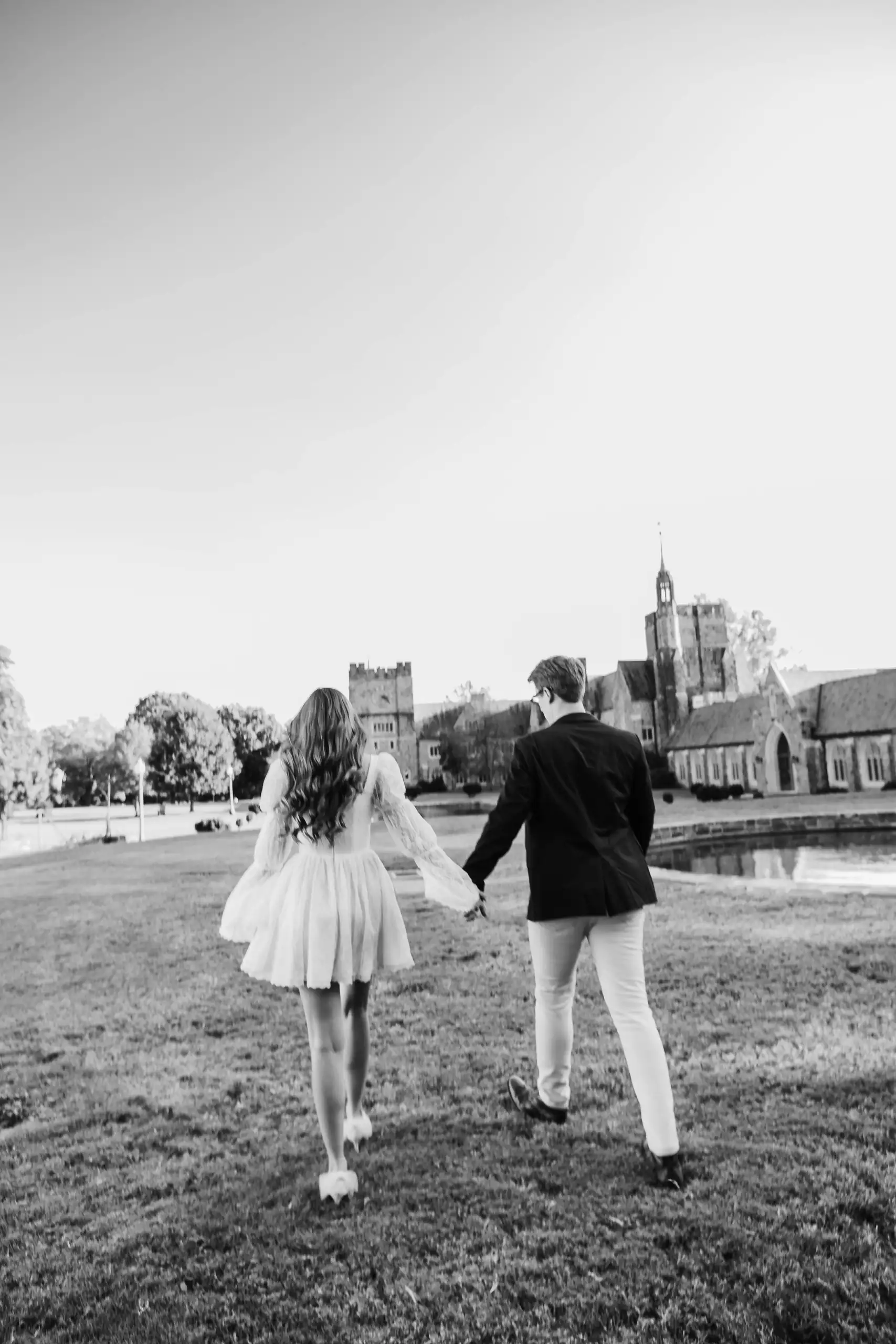 Engagement Portraits: walking together toward the towers, in black and white, during their engagement session at Berry College in Rome, GA