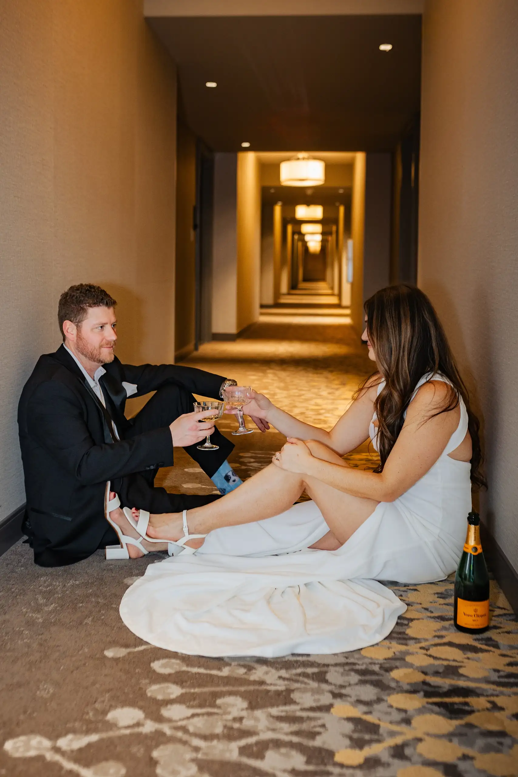 Engagement Portraits: a picnic on the hotel corridor floor with champagne, during their engagement session at the Hotel at Avalon in Alpharetta, GA