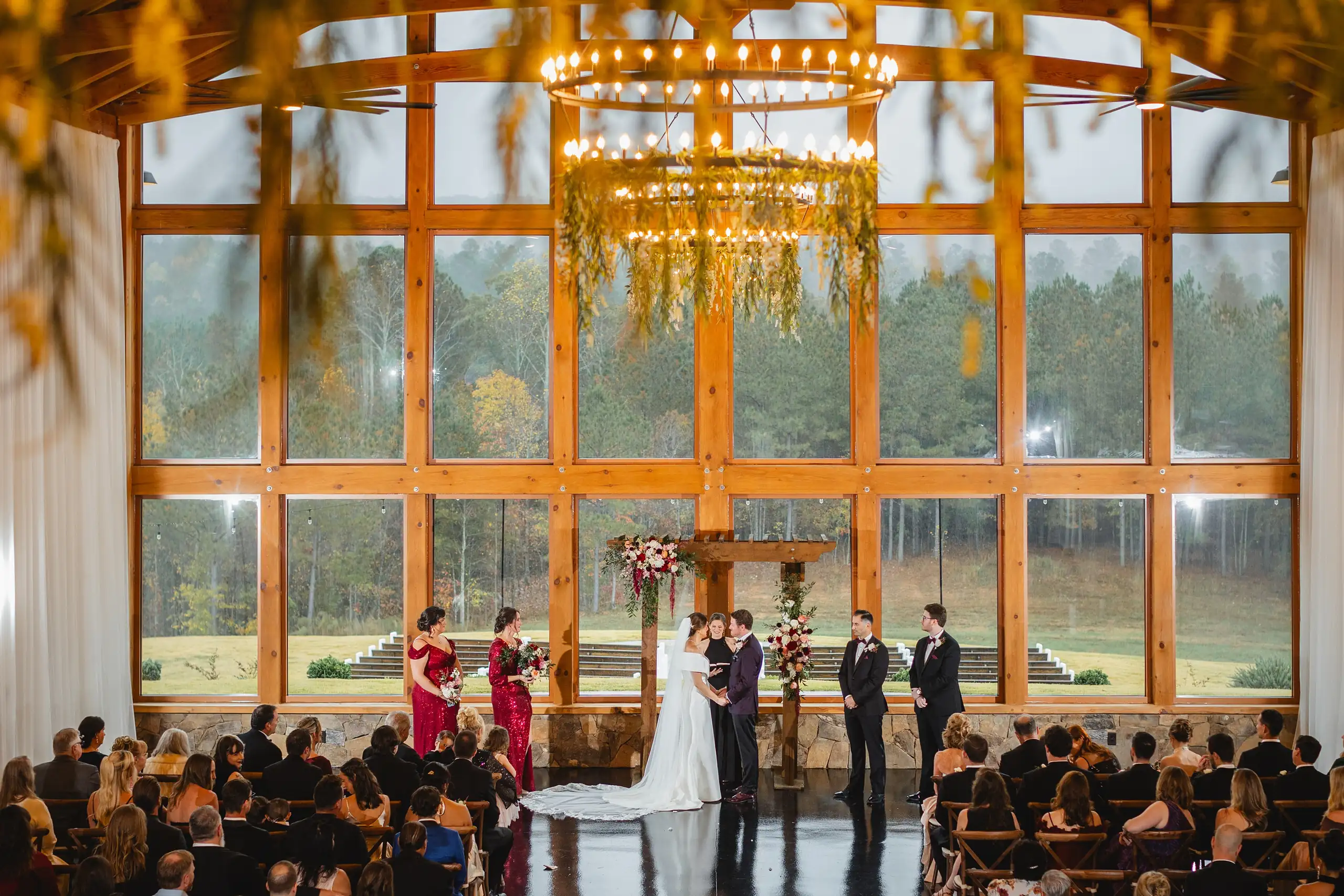 Wedding Ceremony: the ceremony below the chandelier and the glass gable, at their wedding at The Venue at Sharp Mountain in Jasper, GA